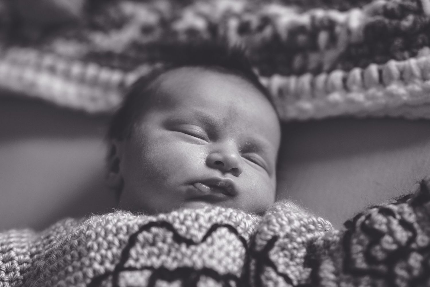 Black and white portrait of peaceful sleeping newborn in knitted clothing.