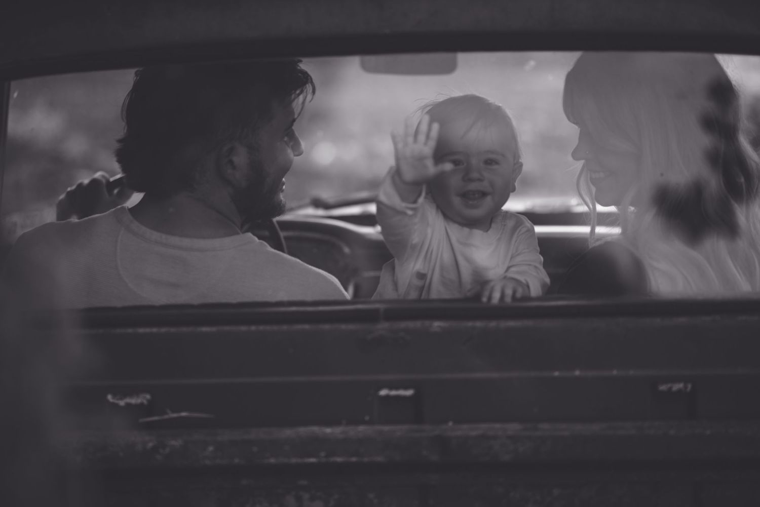 Black and white photo capturing a tender family moment through a car window.