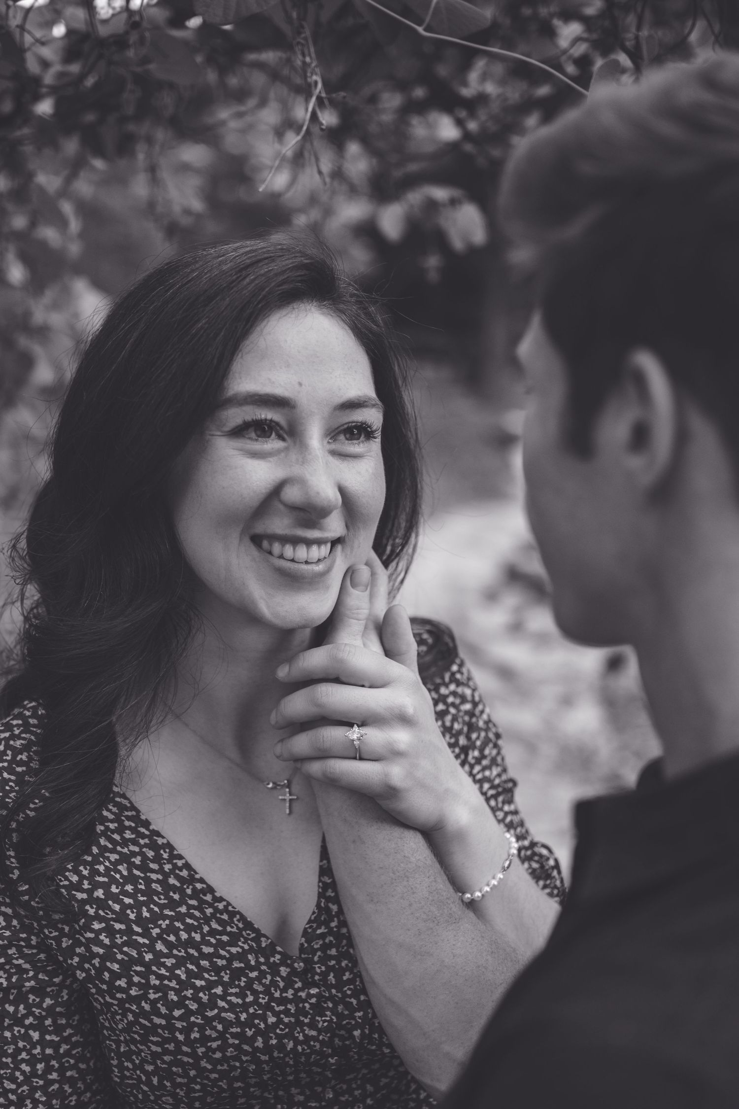 Black and white photo of a smiling woman holding hands with a man outdoors, wearing a cross necklace.