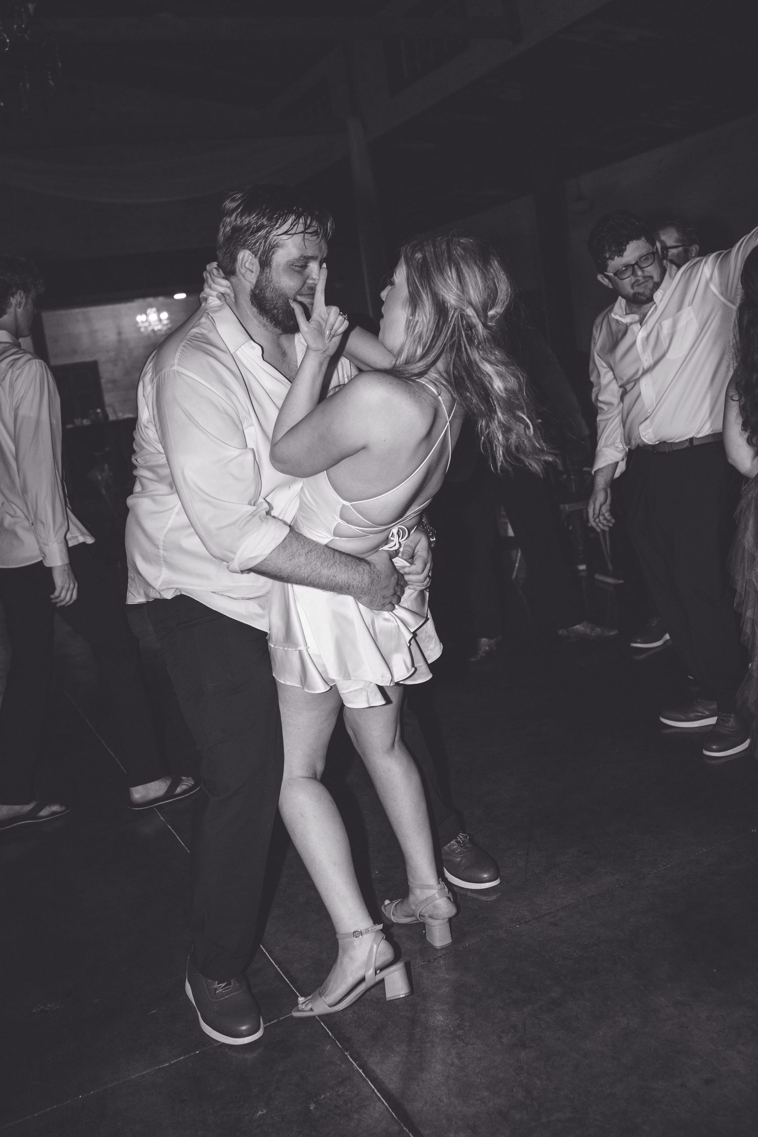Black and white photo of a couple dancing closely at a party, surrounded by other guests on the dance floor.