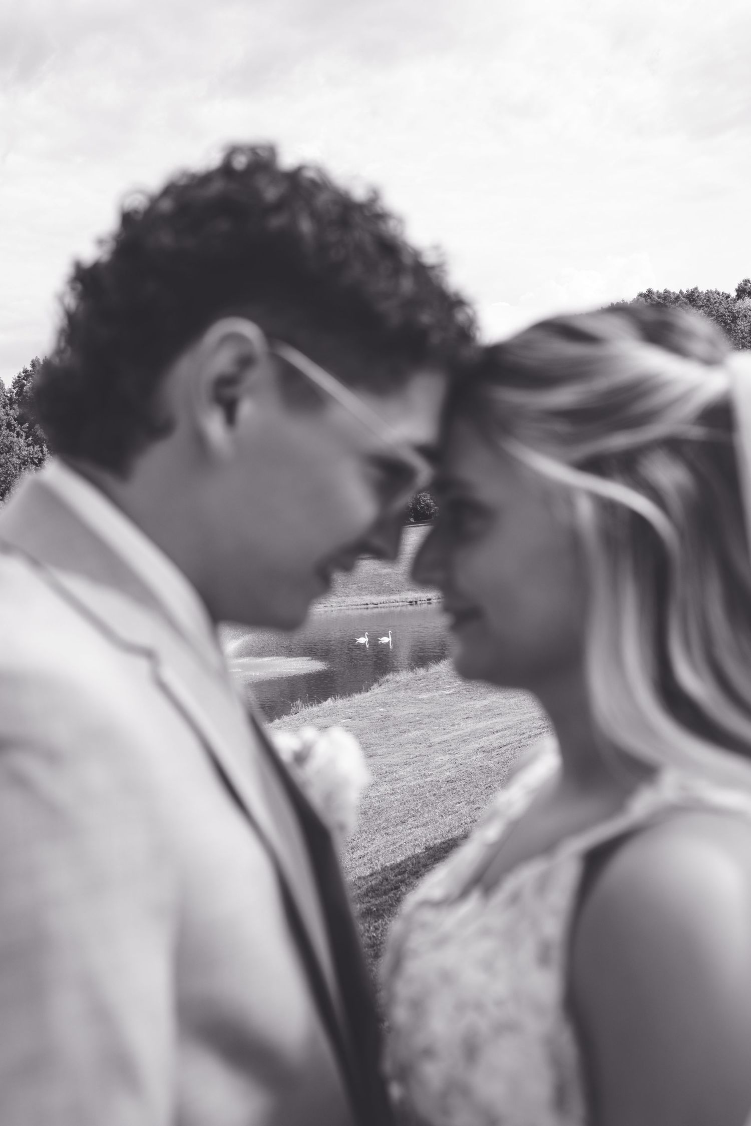 Black and white romantic photo of bride and groom touching foreheads tenderly at outdoor wedding ceremony.