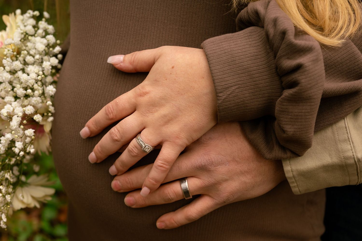 Close-up view of hands wearing a sparkling engagement ring against a backdrop of delicate white spring blossoms.