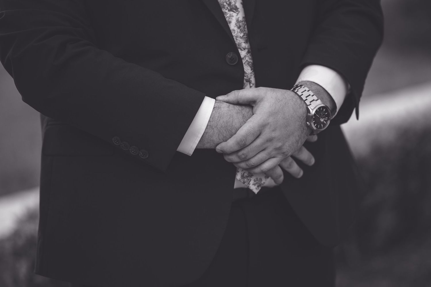 Black and white photo of a man in a suit clasping his hands together, wearing a stylish wristwatch.