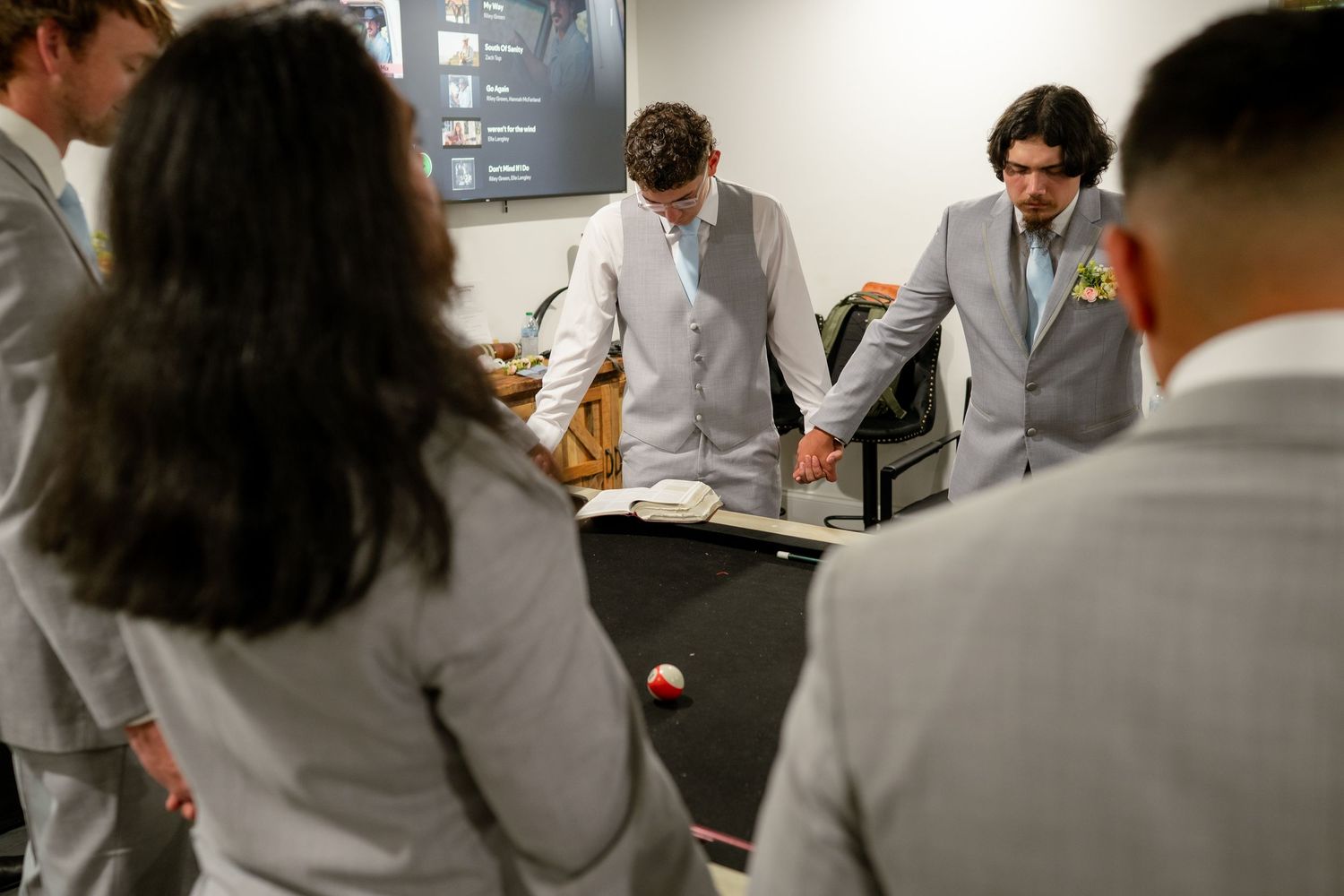 Groomsmen in gray suits gather around a pool table during wedding day preparations.