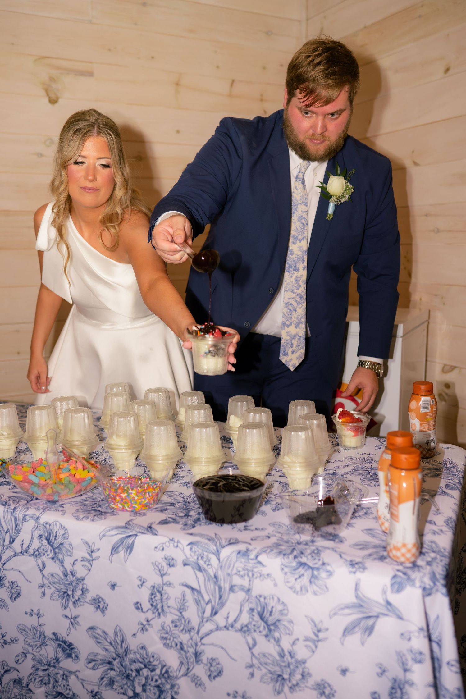 Bride and groom serving ice cream sundae bar at wedding reception dessert table.