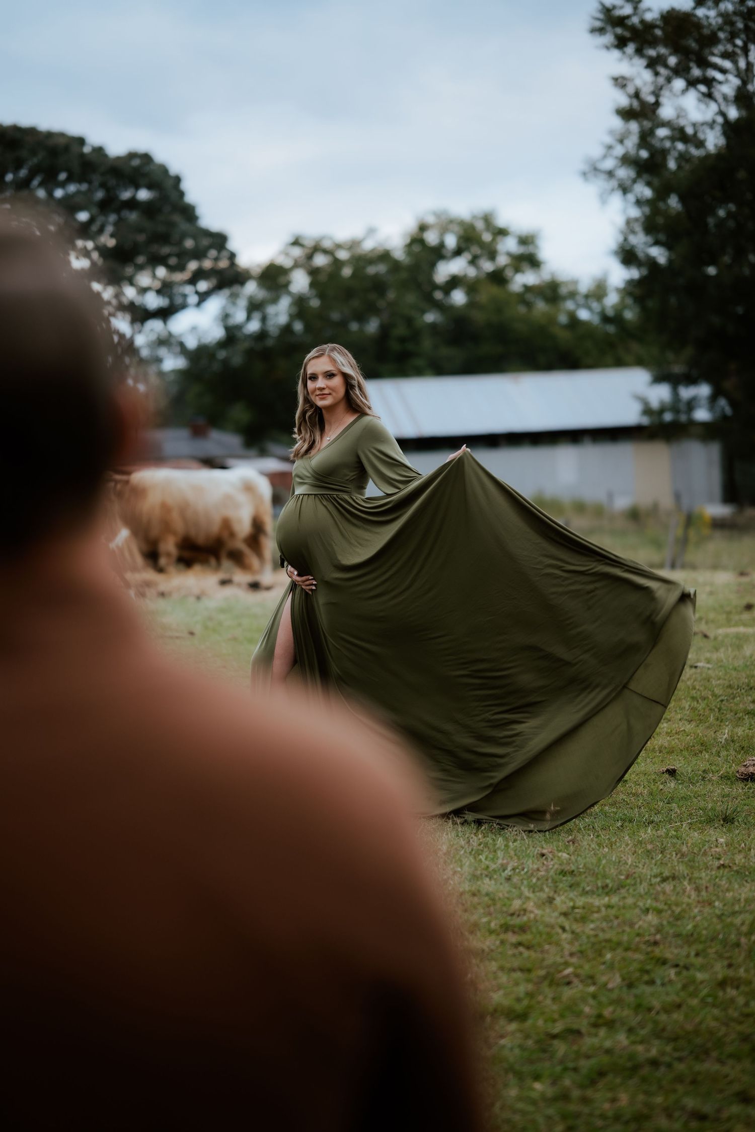 Side angle of maternity shoot with flowing dress movement in farm setting.