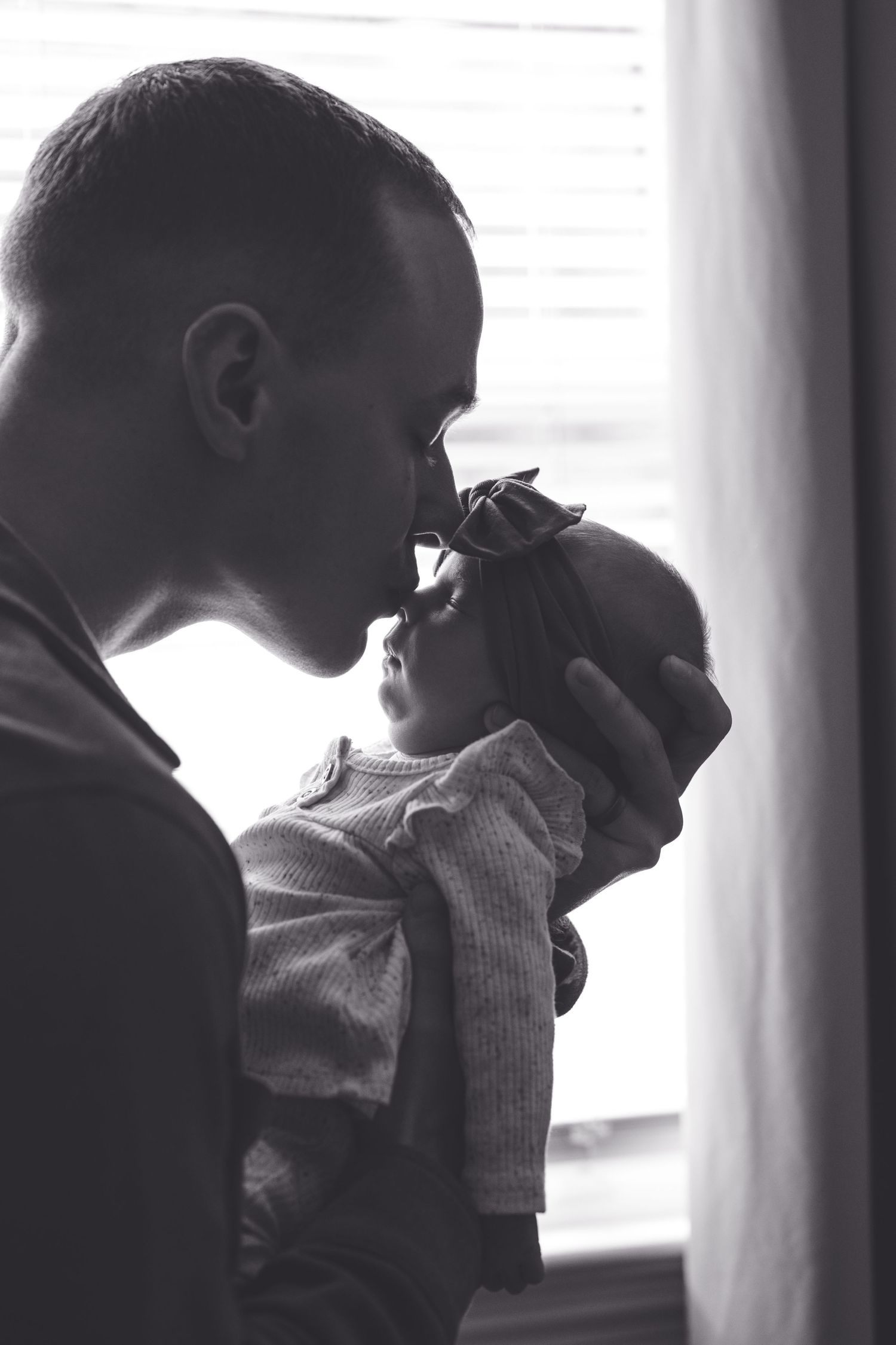 Silhouette of parent and baby sharing an intimate moment by window light.