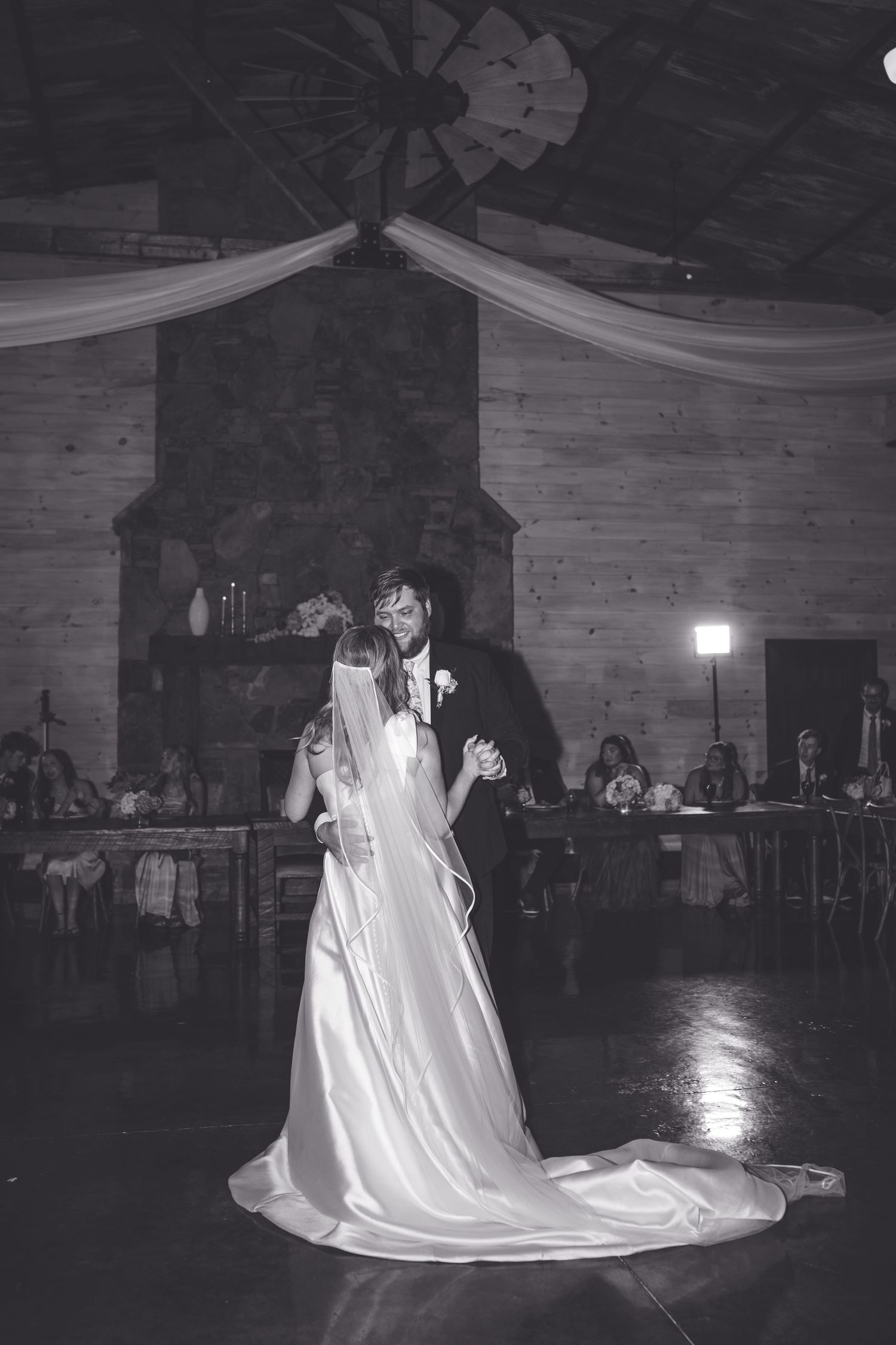 Black and white photo of bride and groom sharing their first dance at a rustic wedding reception venue.