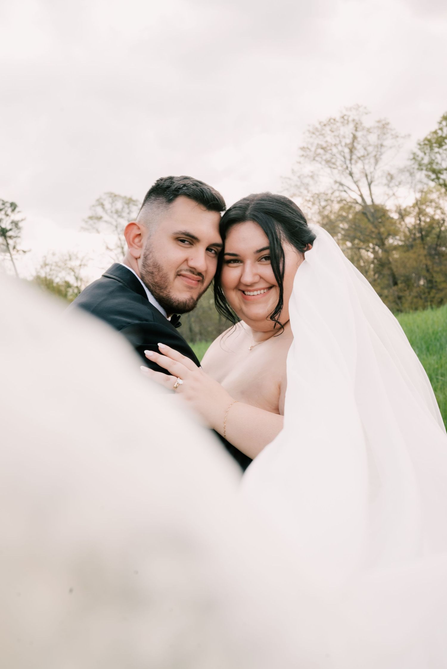 A romantic wedding portrait captured outdoors with a flowing white veil and natural scenery in soft focus. North Carolina