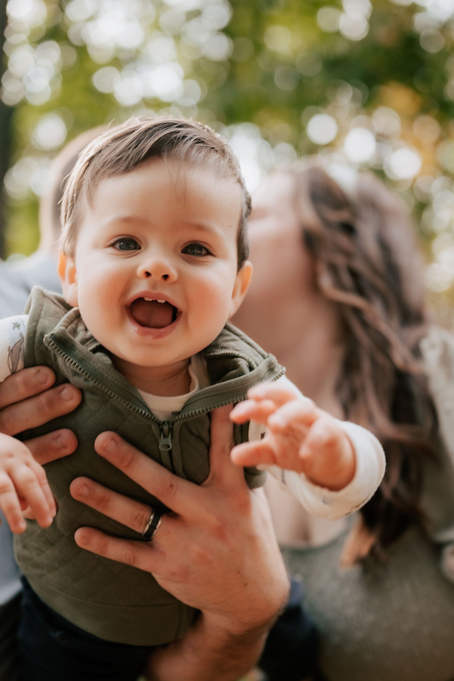 Joyful baby laughing while being held up outdoors in natural lighting.