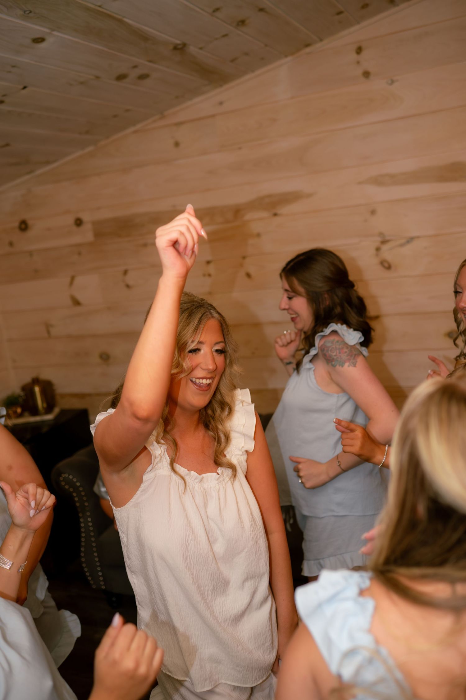 Bride dancing joyfully with arm raised at rustic wood-paneled wedding reception.
