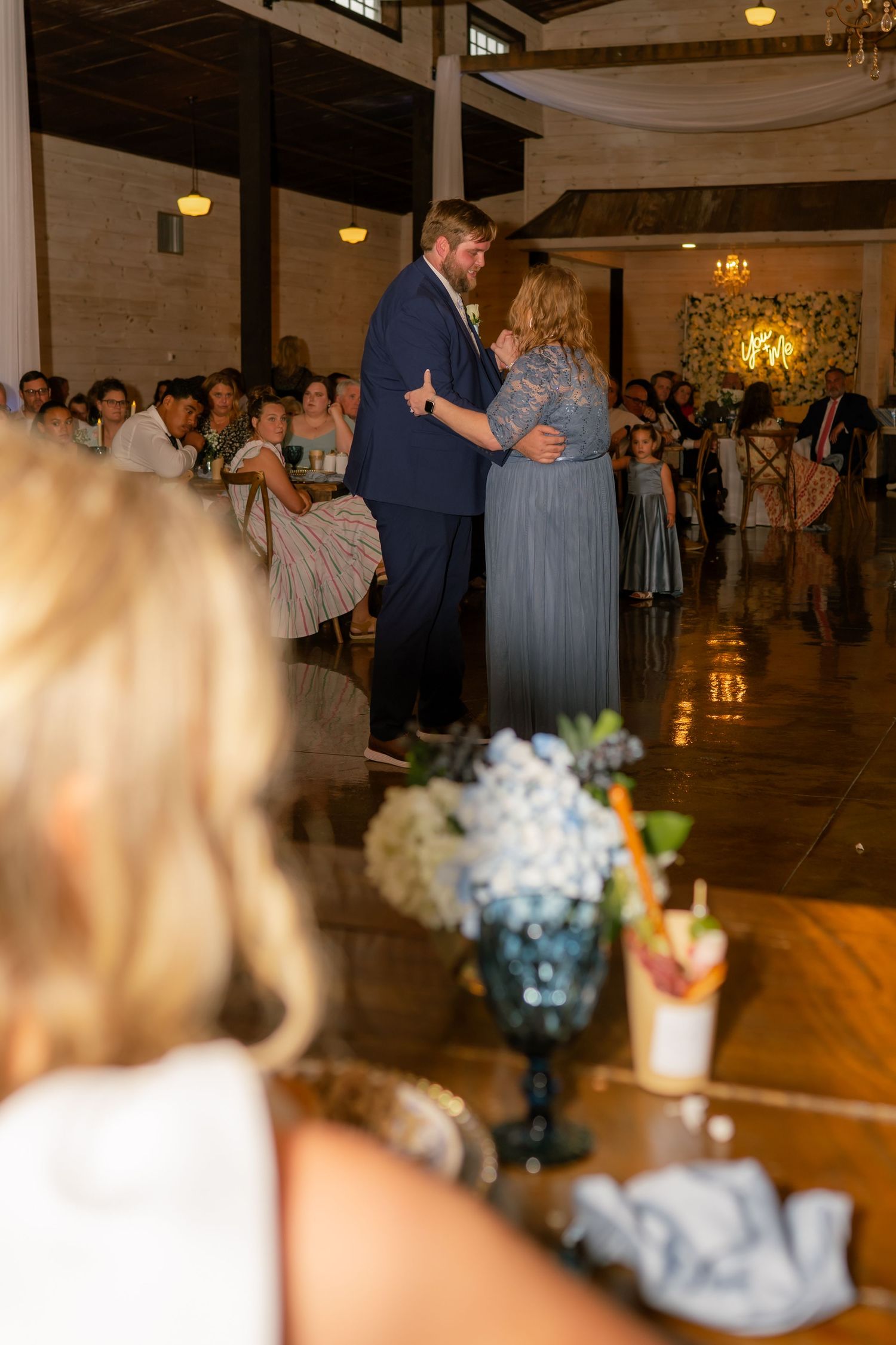 Groom shares a mother-son dance at elegant wedding reception while guests watch.
