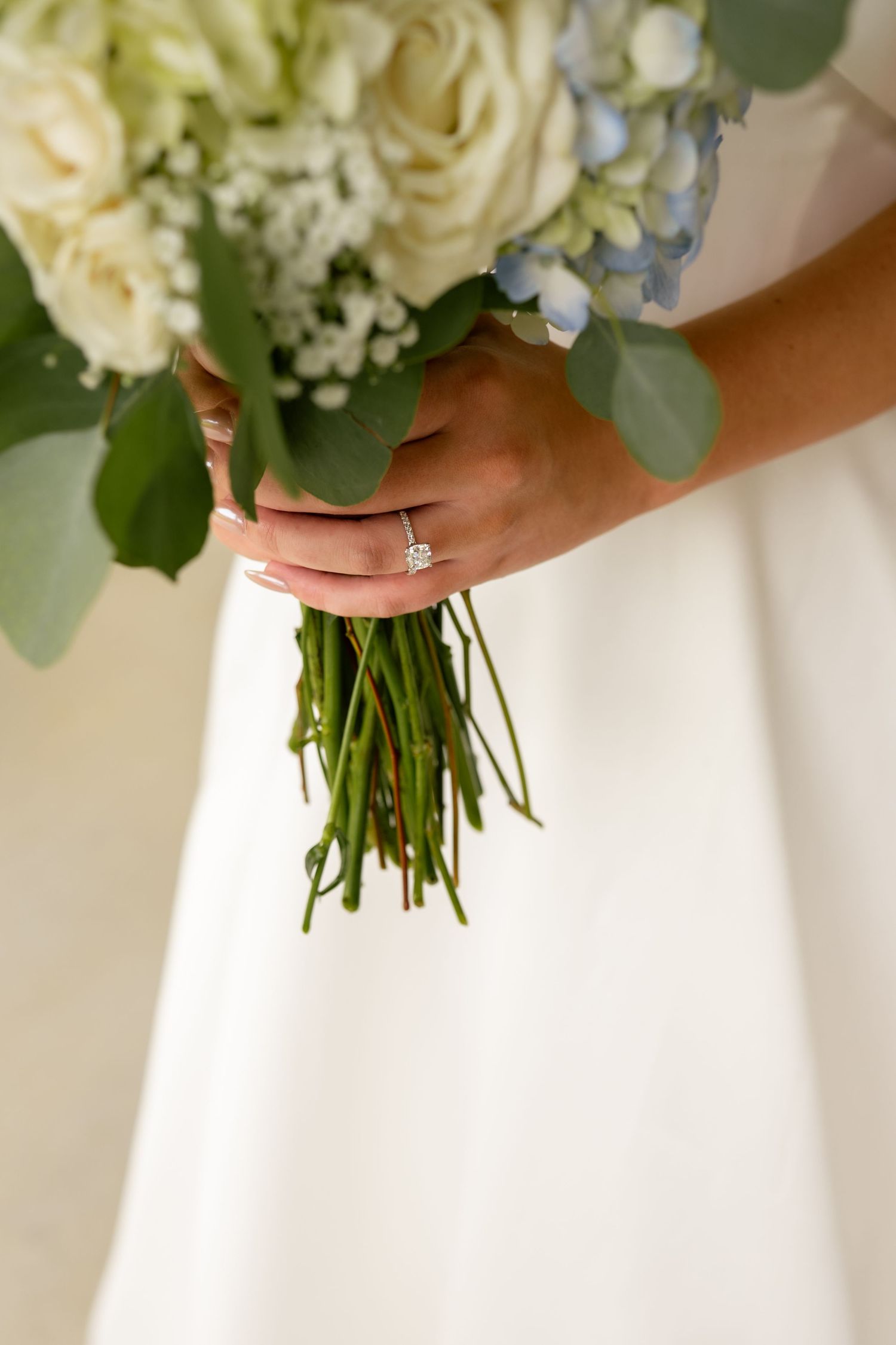 Bride holding white and blue wedding bouquet with diamond engagement ring visible.