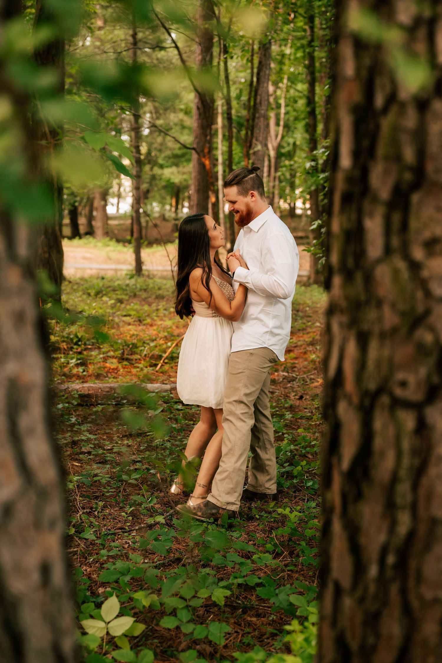 A romantic couple in light-colored outfits share an intimate moment among trees in a wooded area during daytime in North Georgia .
