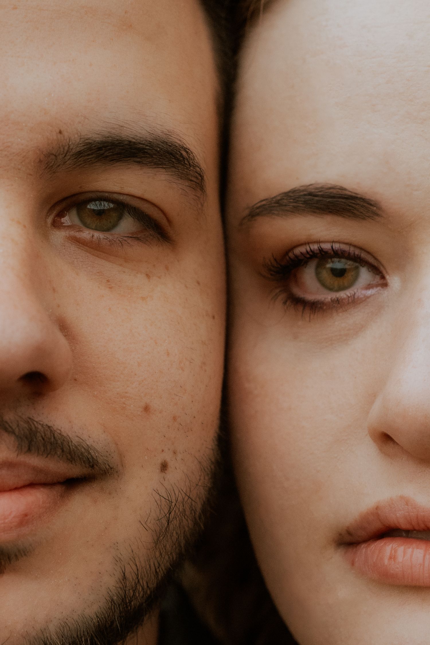 Intimate close-up portrait showing half faces of a couple with warm-toned lighting.