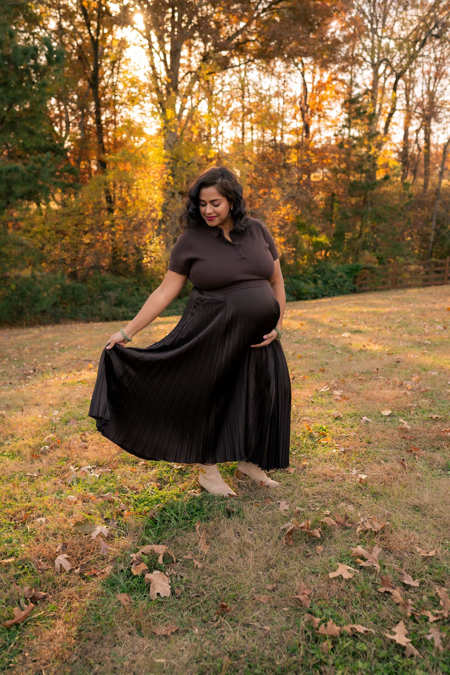 A person in a flowing black dress poses gracefully on an autumn hillside during golden hour sunset.