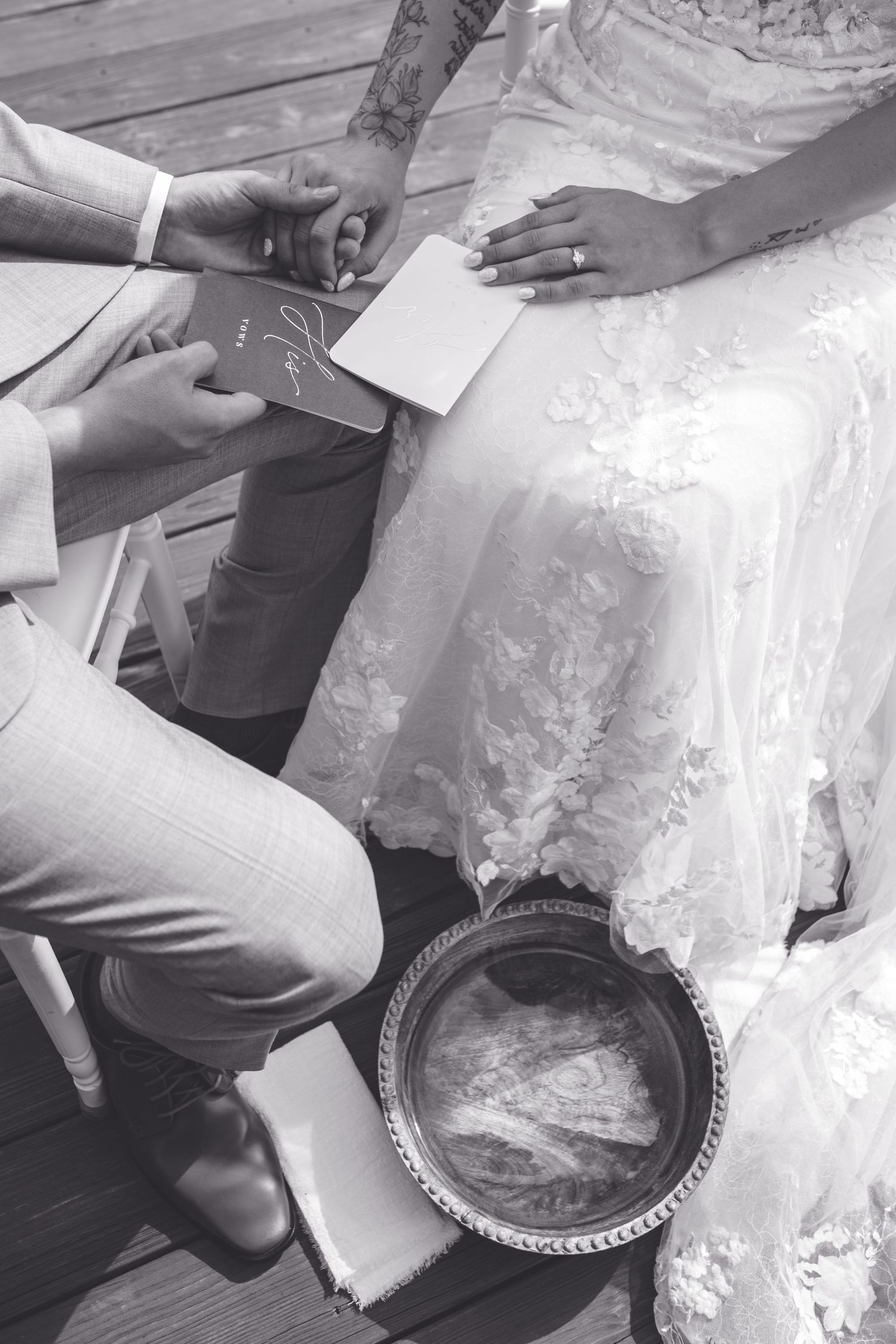 Black and white close-up of bride and groom exchanging vows, holding cards over a ceremonial wash basin.