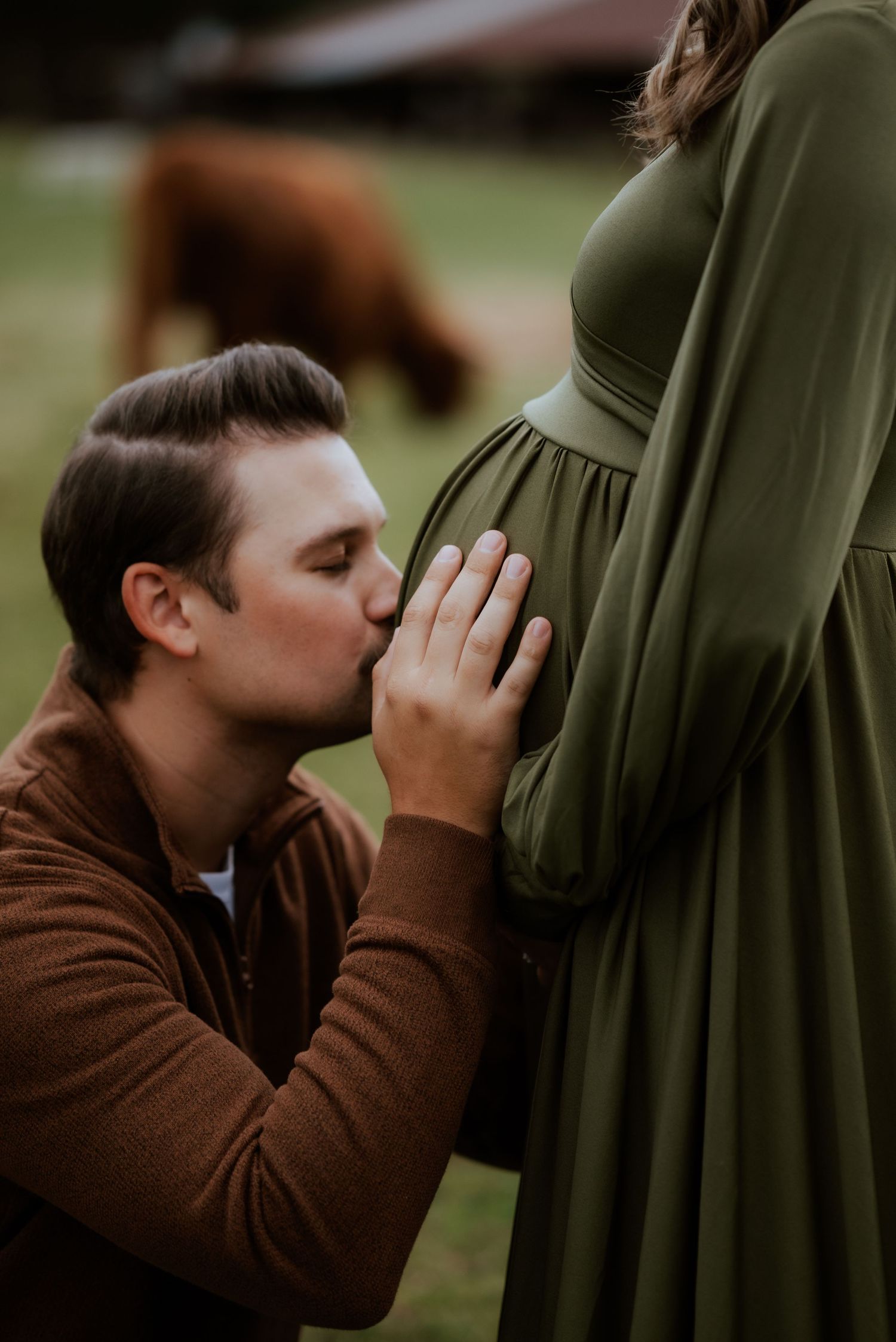 Intimate maternity moment outdoors with couple in green dress and brown sweater.