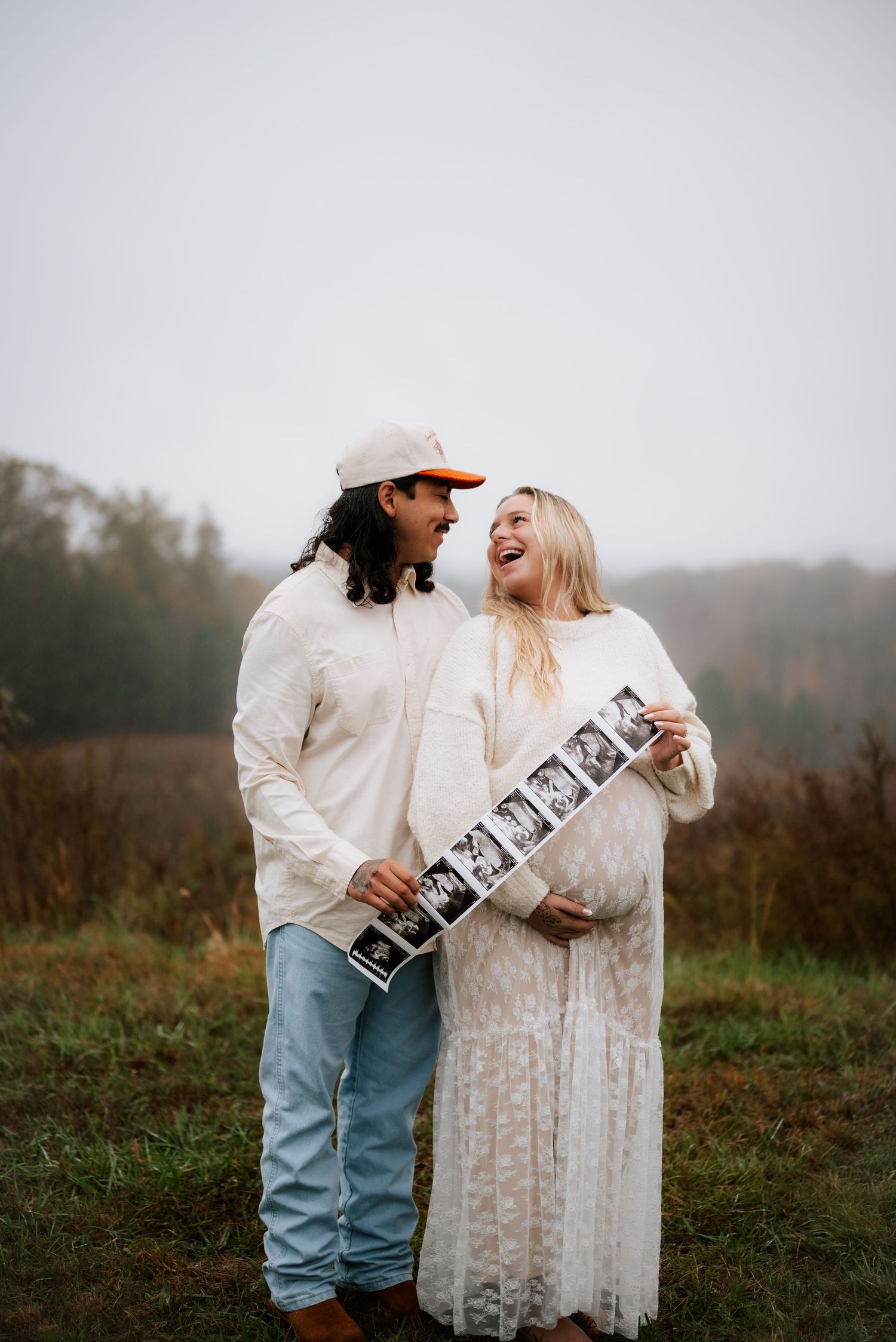 Joyful couple in coordinated white outfits sharing pregnancy moments with ultrasound strip.