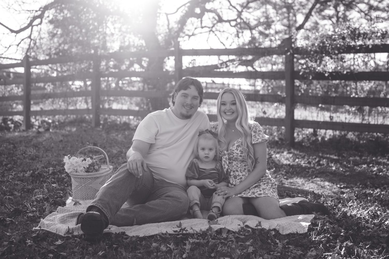 A family enjoys a picnic together on a blanket near a rustic wooden fence.