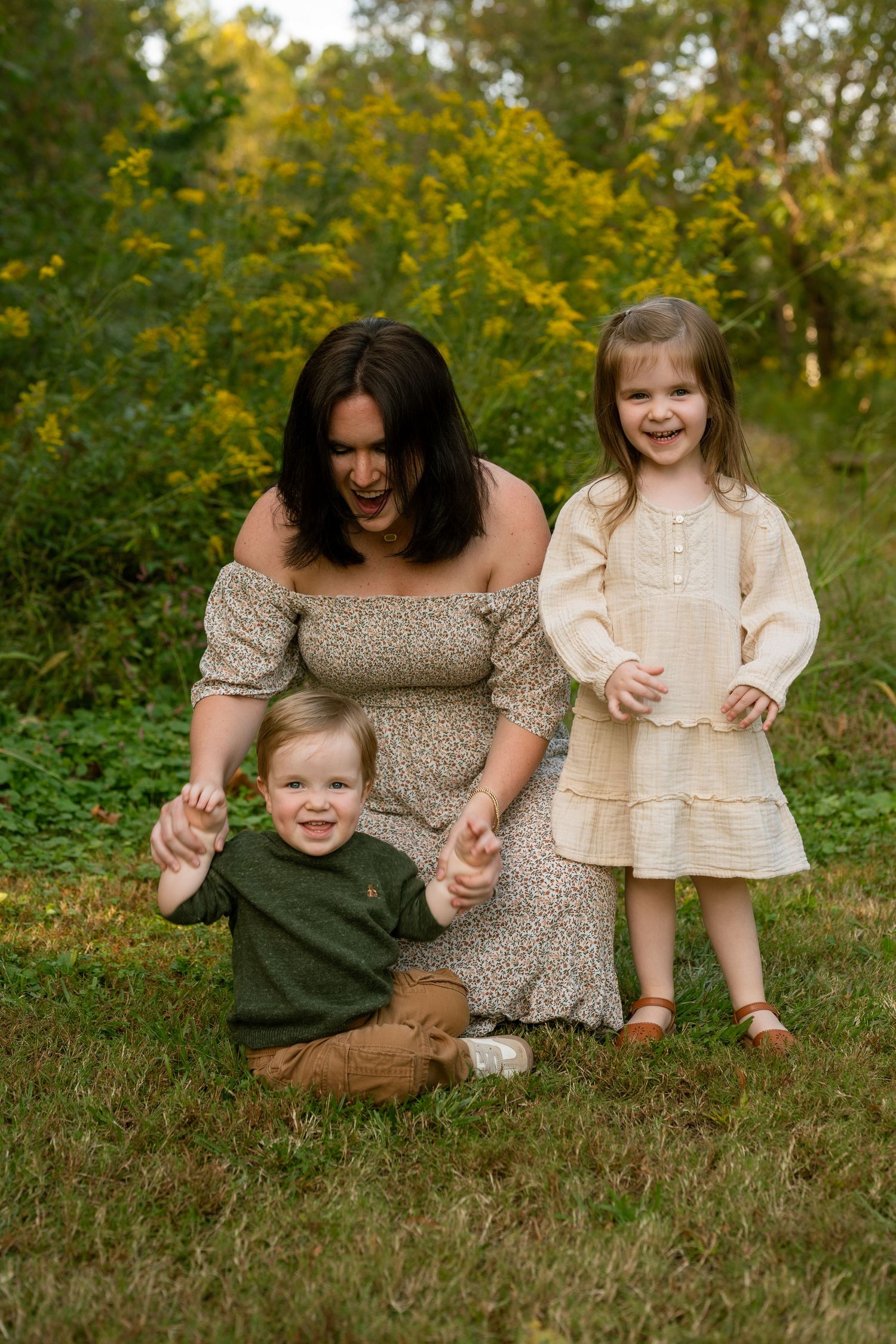 Family in coordinating earth-toned outfits sits together on grass during golden hour outdoor photo session.