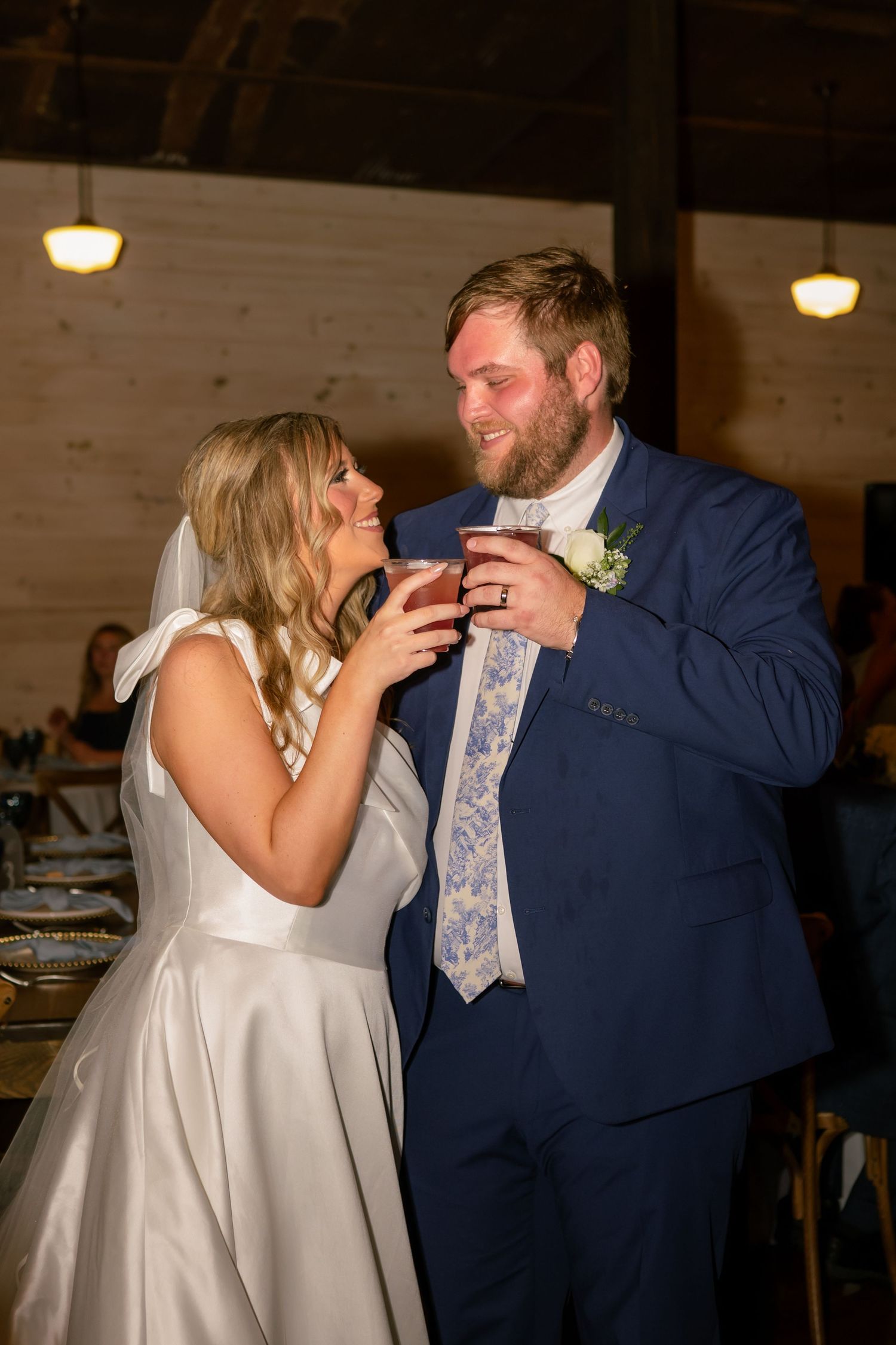 Bride and groom in navy suit share a drink and laugh together at wedding reception.