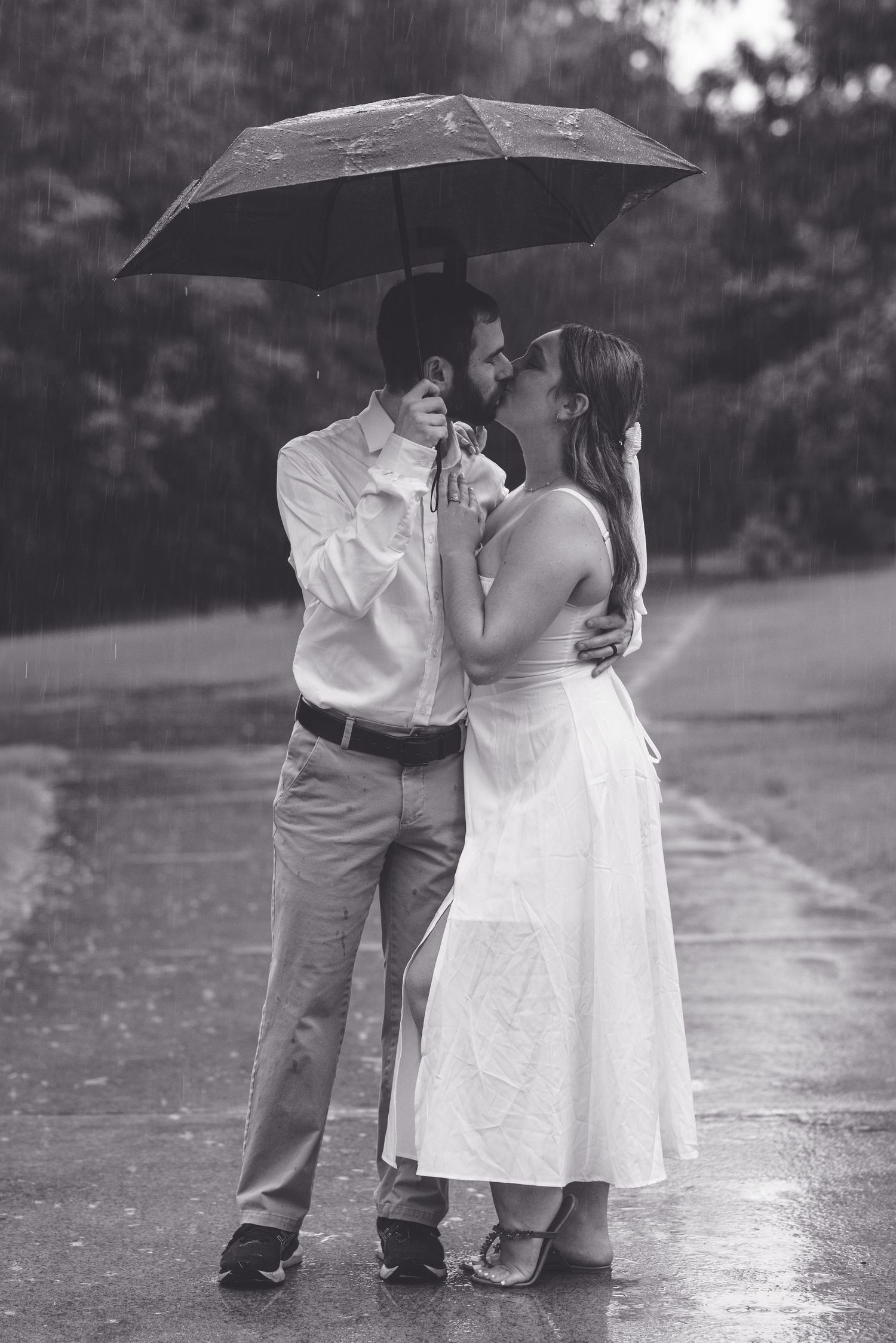 A romantic black and white photo of a couple sharing an intimate moment under an umbrella in the rain.
