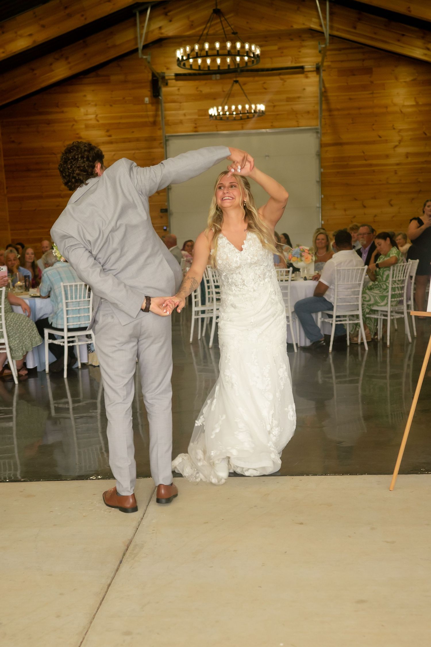 Bride and groom share first dance in rustic barn wedding venue while guests watch from decorated tables.