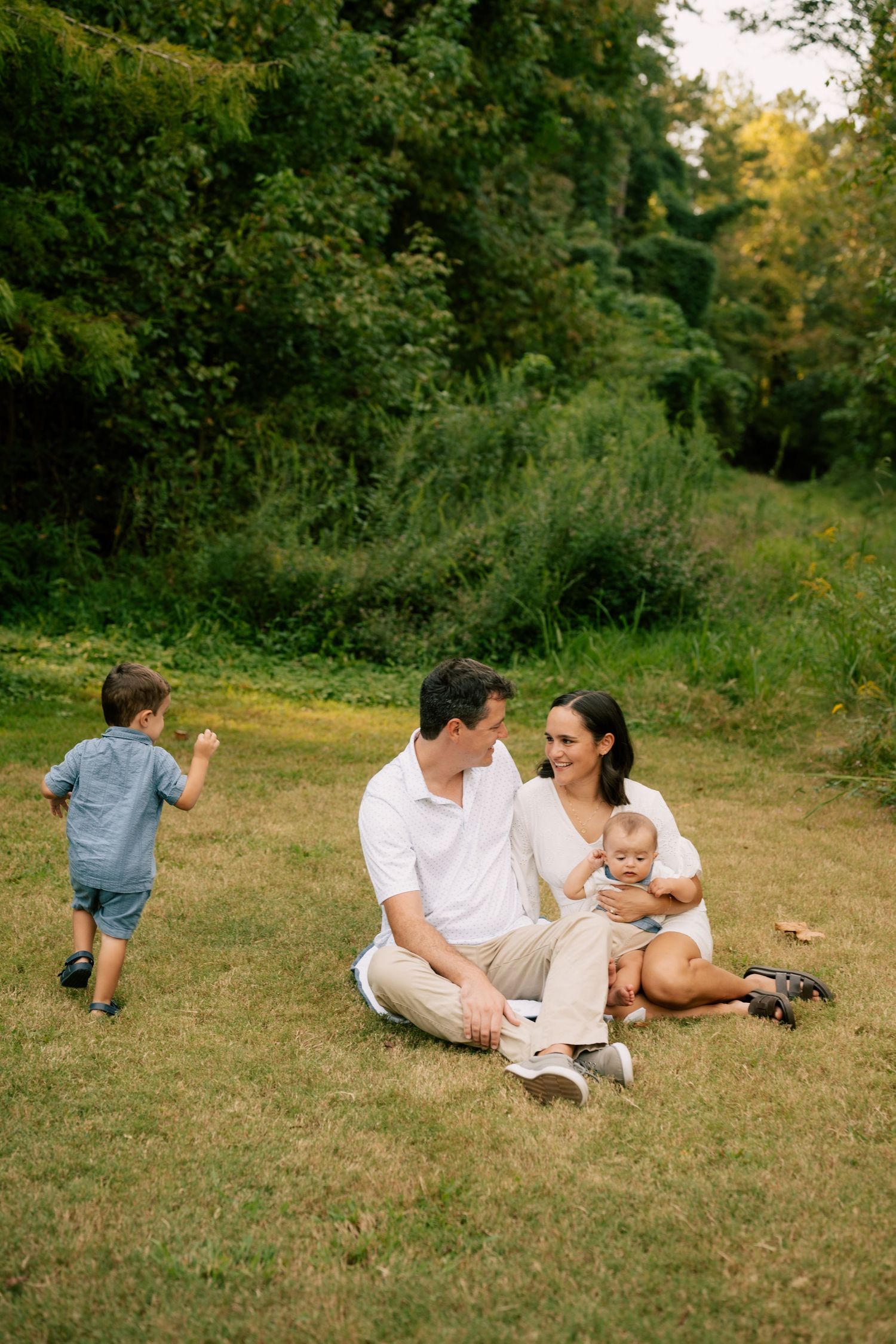 Family enjoying a relaxed summer afternoon picnic on grassy field with trees in background.