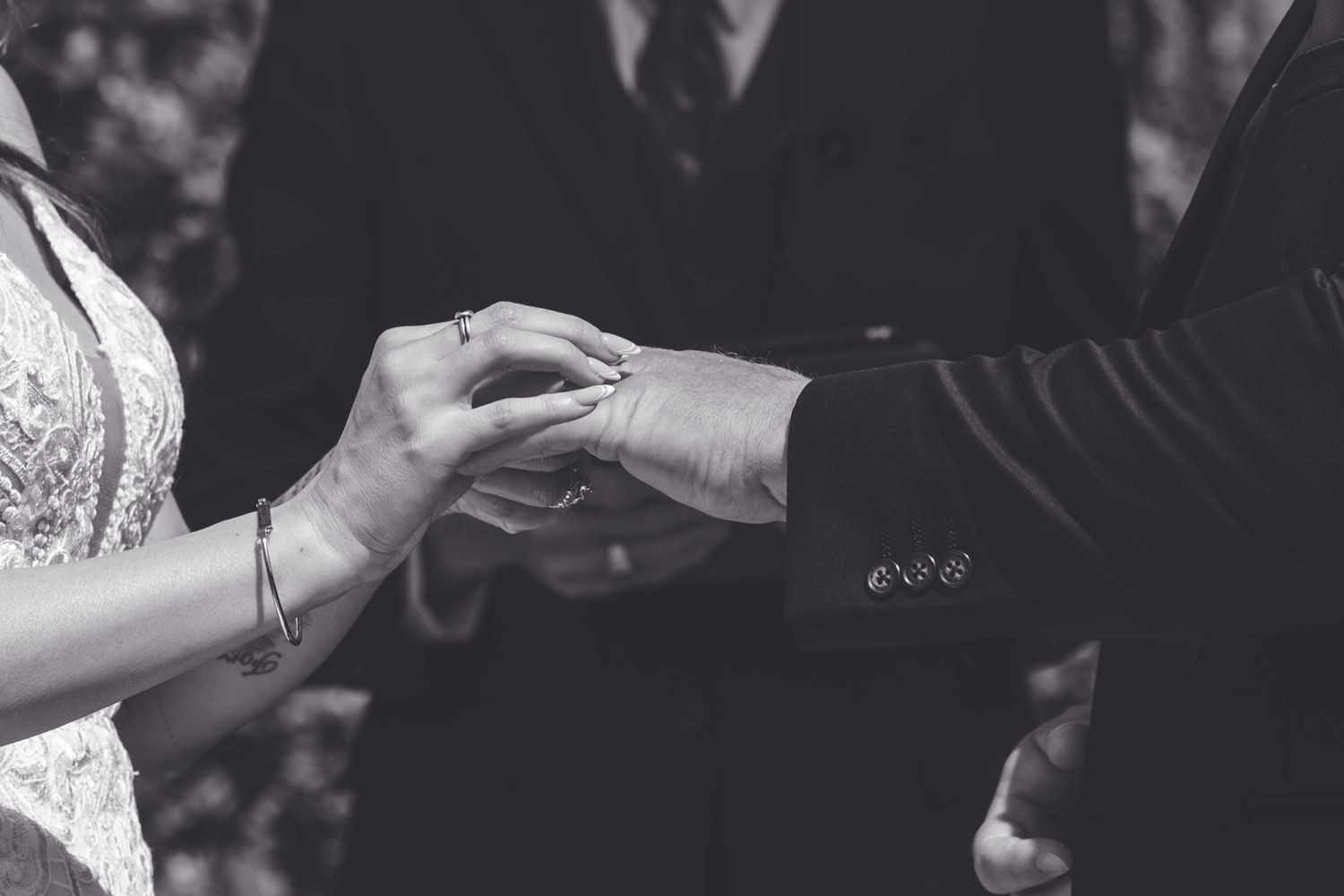 Black and white photo of a couple exchanging wedding rings during a ceremony, close-up of hands.