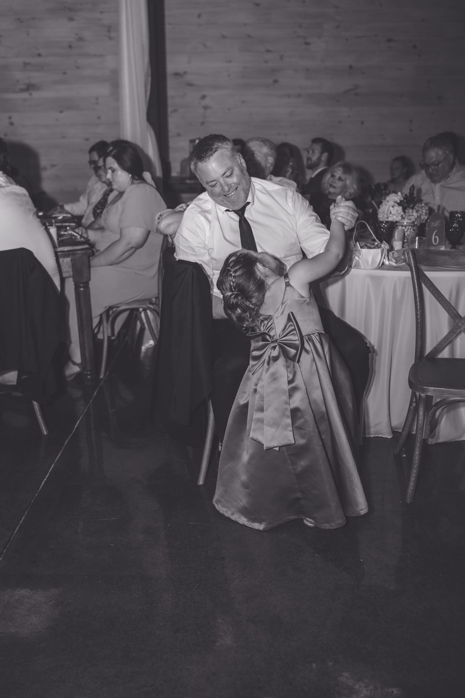 Black and white photo of a man dancing with a flower girl at a wedding reception.