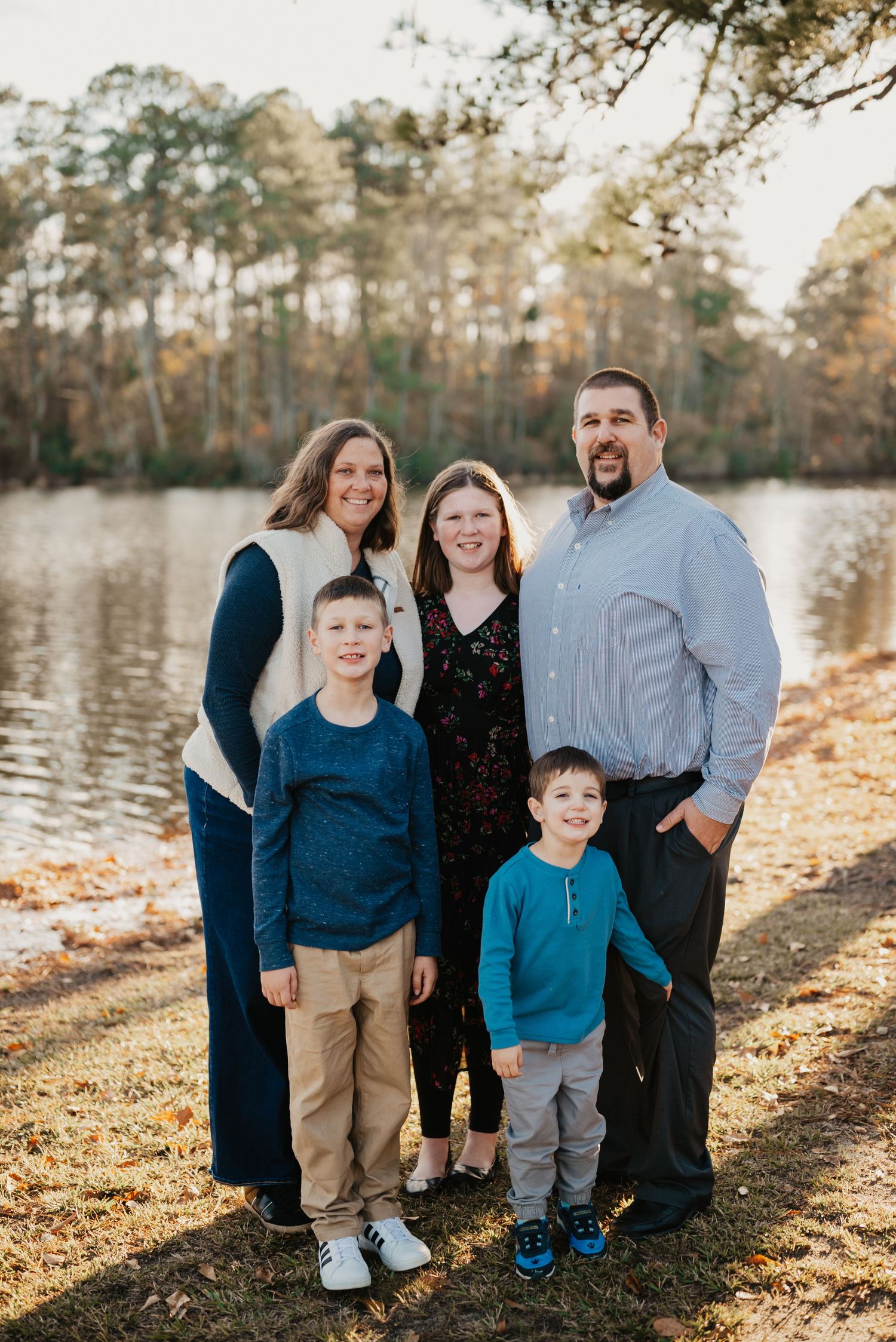 Family portrait of five people standing by lake during golden hour in autumn.