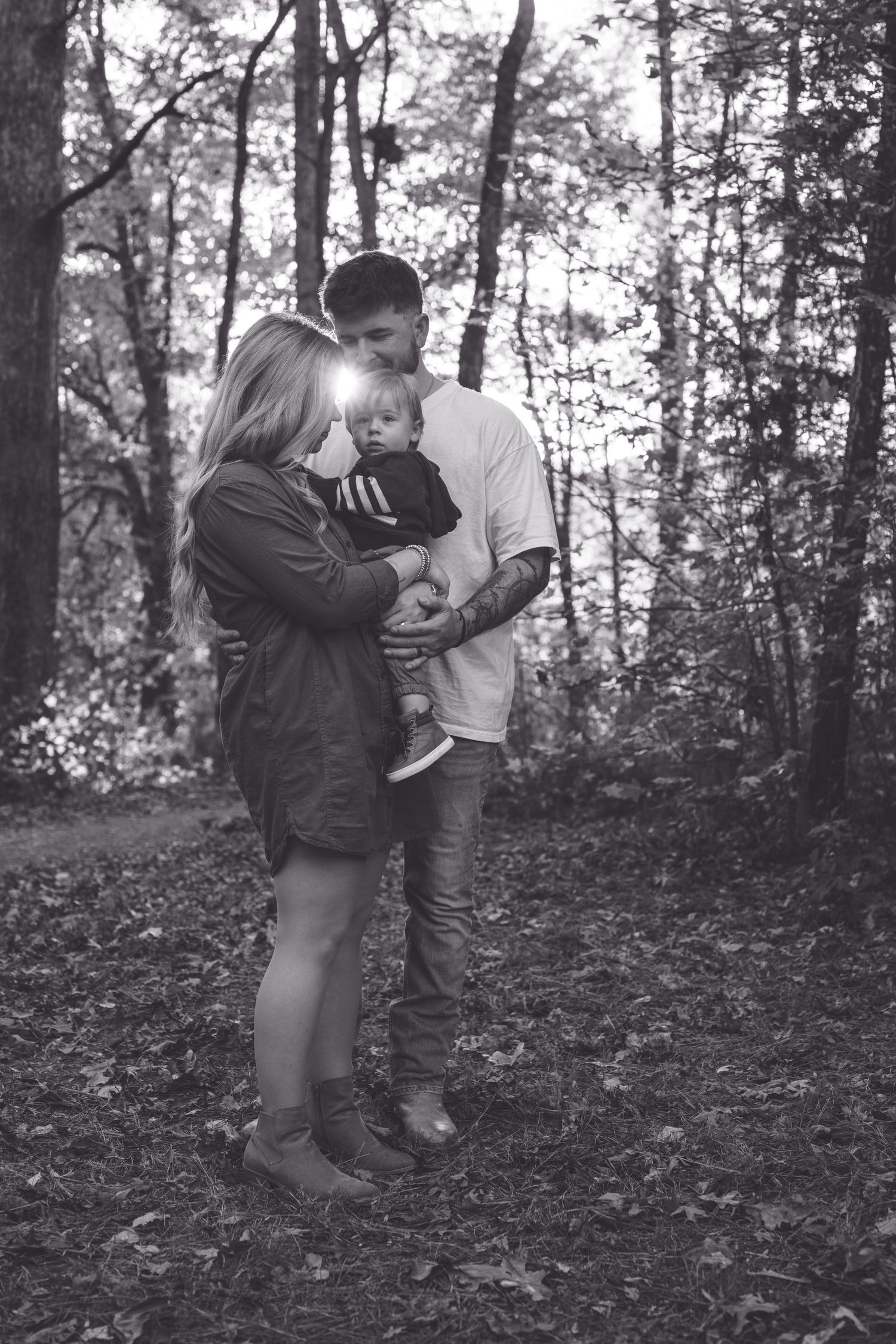 A tender family moment captured in black and white in a wooded forest setting.