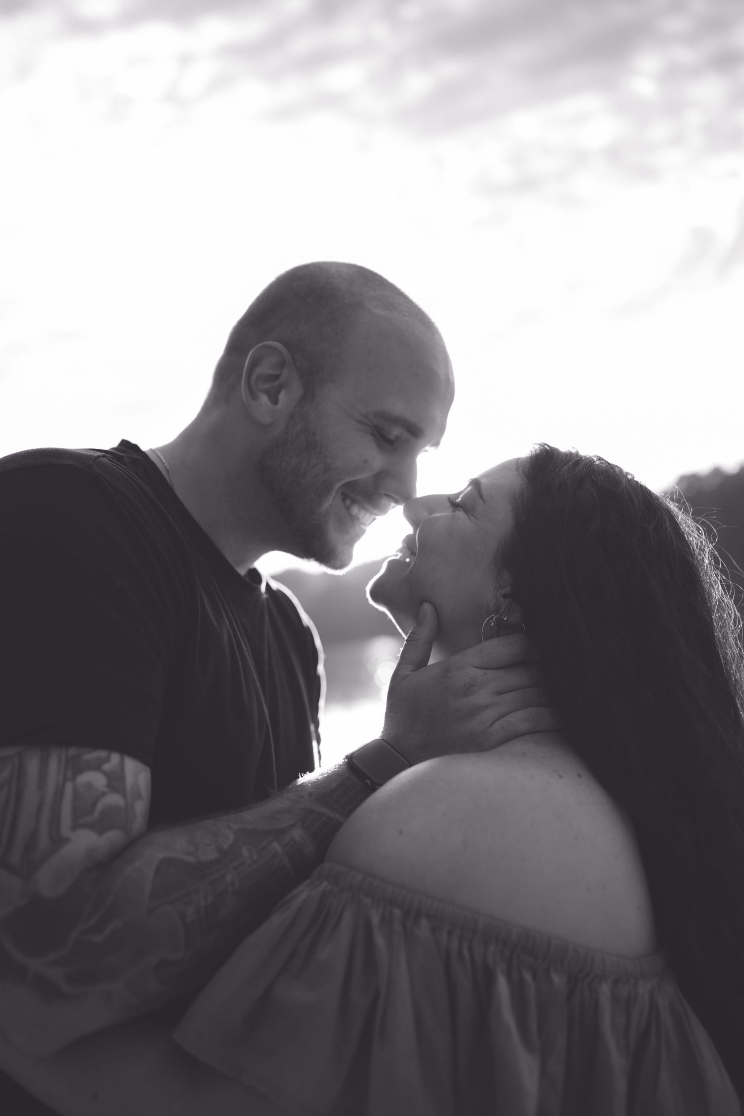 Black and white photo of a couple smiling and gazing at each other outdoors, man gently holding womans face.