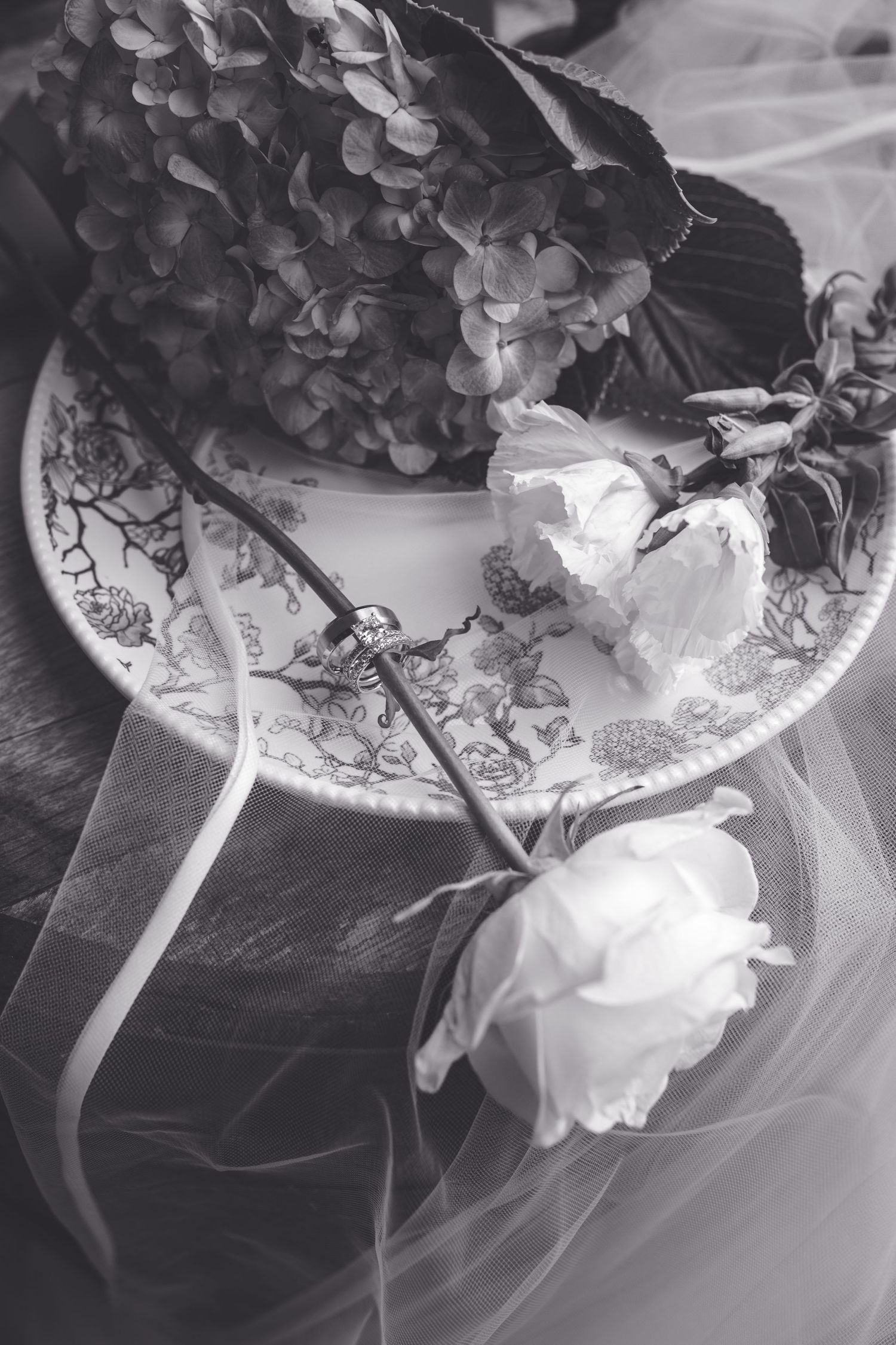 Black and white photo of hydrangeas and white roses on a decorative plate with sheer veil.