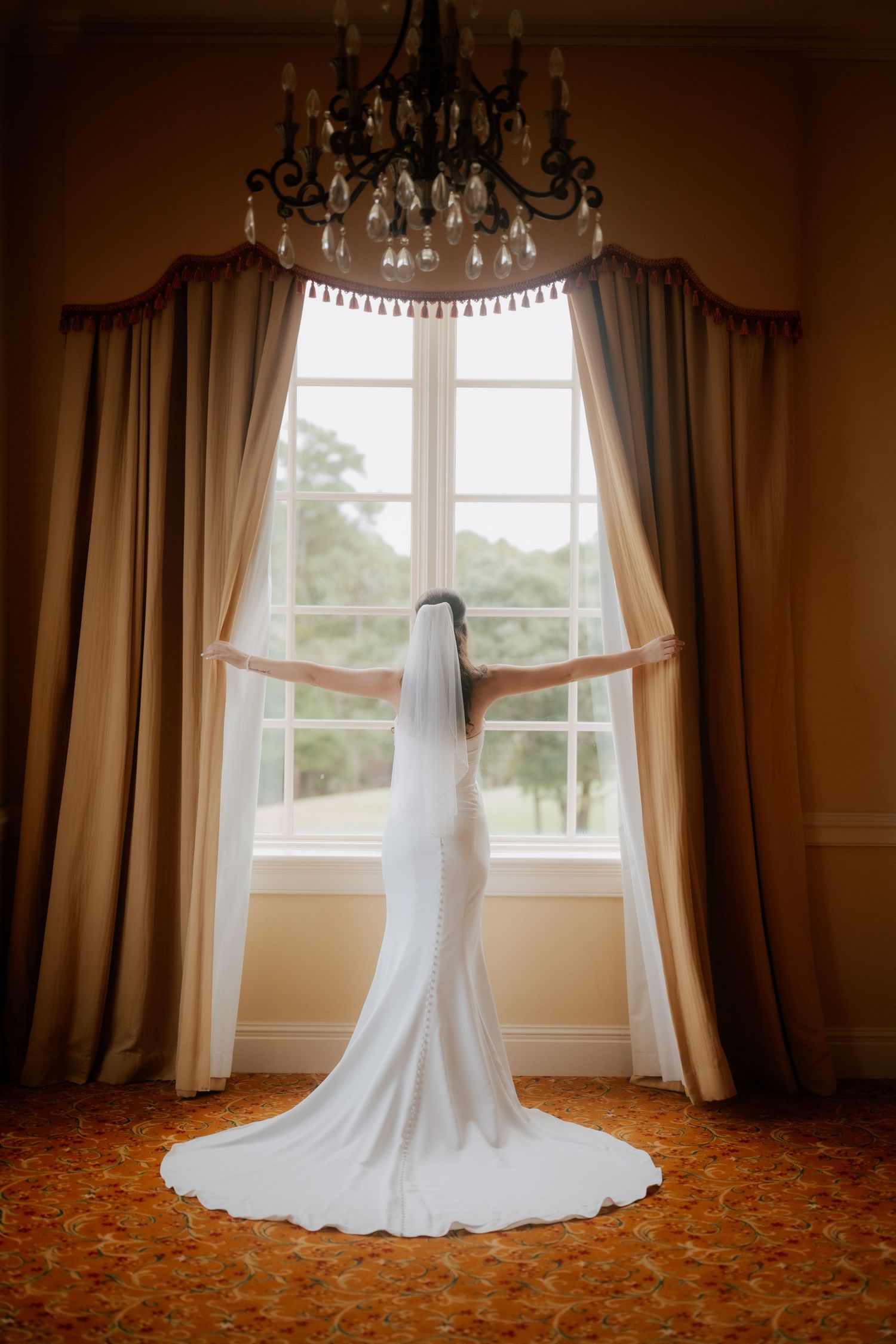 A wedding dress displayed against a window with elegant drapes and chandelier. North Carolina