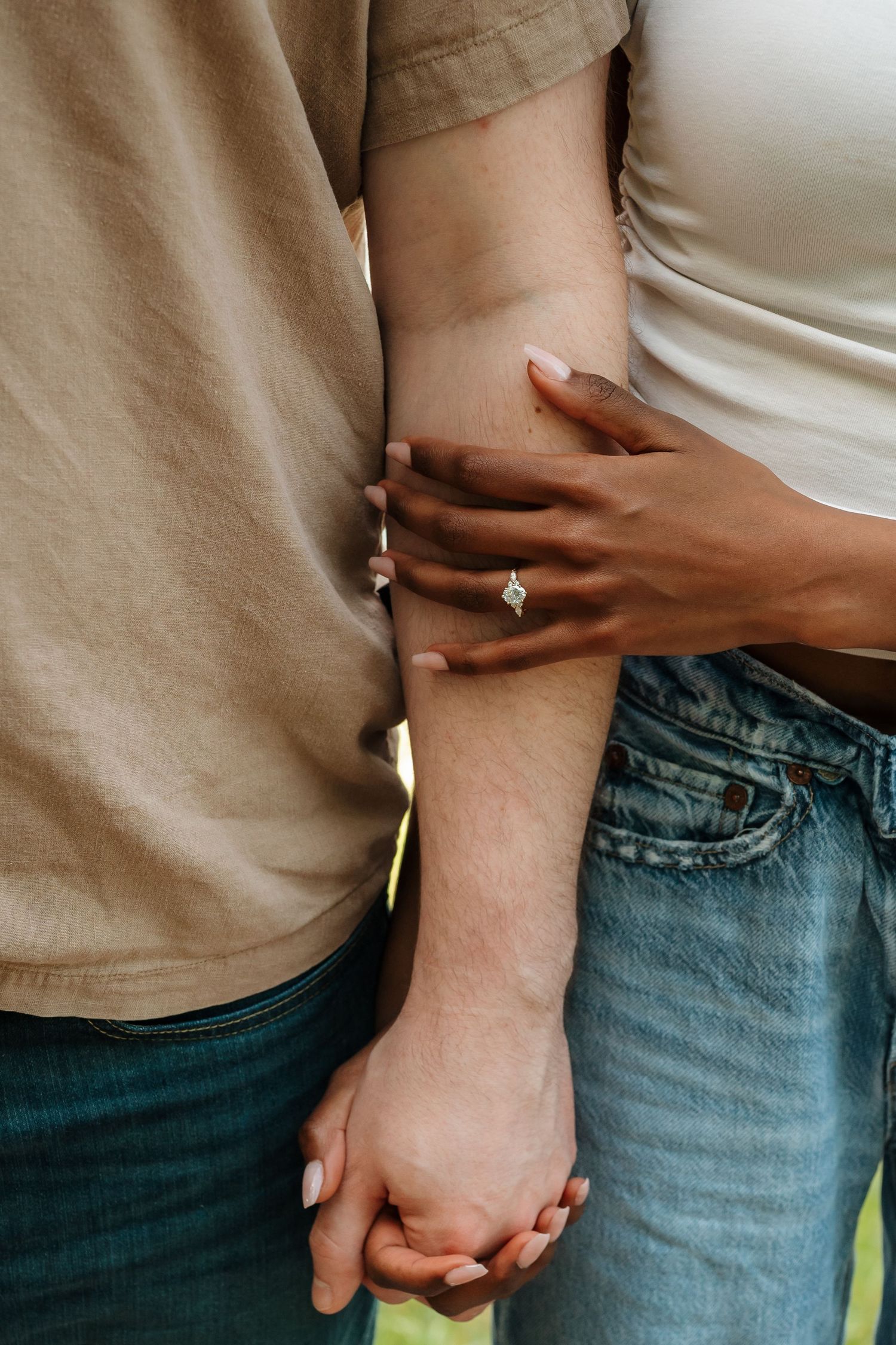 Close-up of two people holding hands intimately while wearing jeans and casual clothing, with rings visible on their fingers. in NC