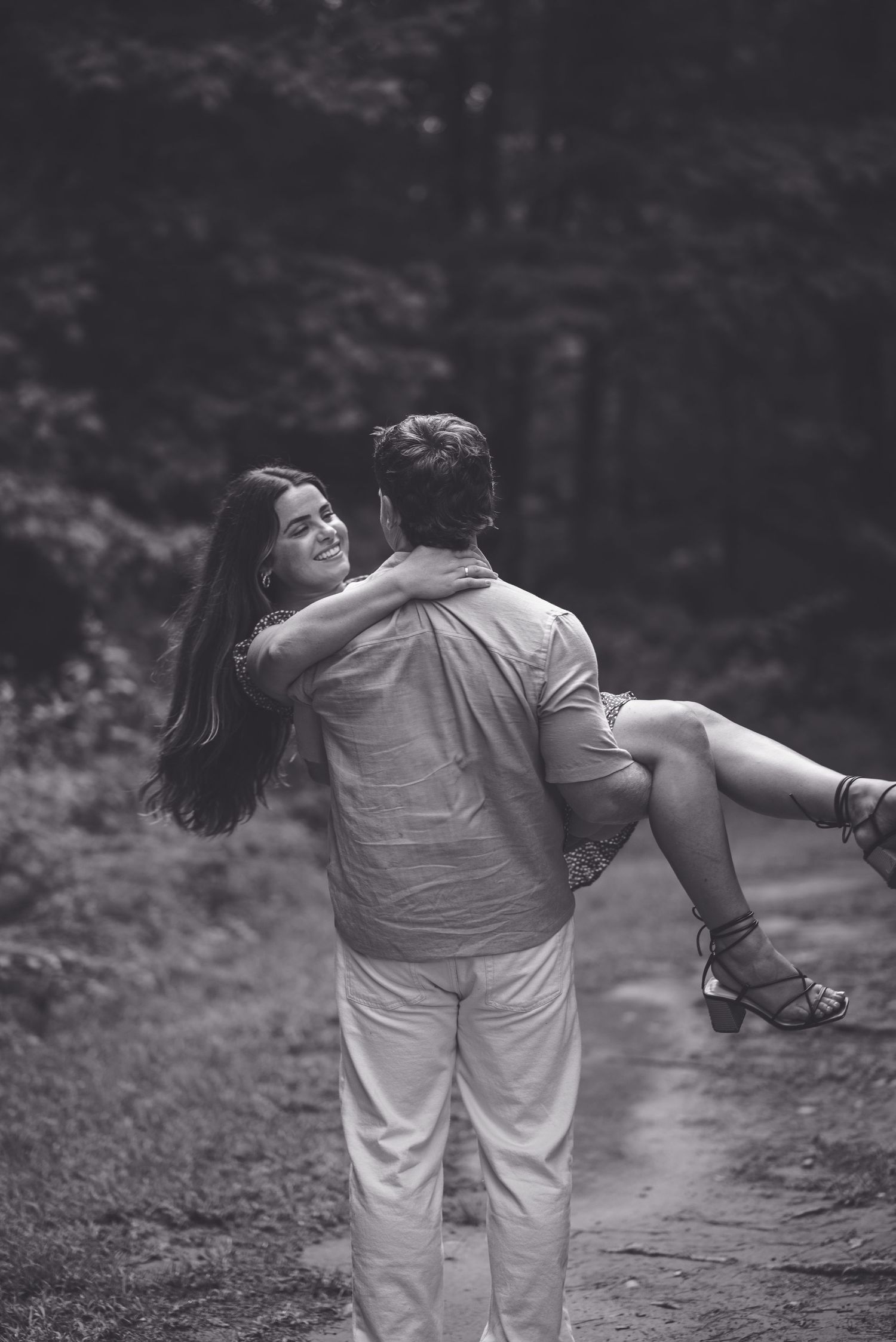 A black and white photo of someone carrying their partner playfully on a woodland path.