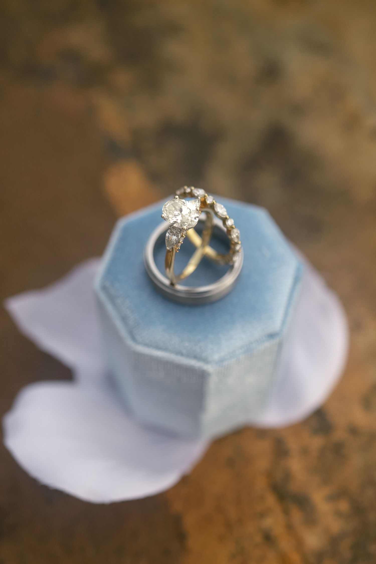 Close-up of diamond engagement ring and wedding bands displayed in a blue velvet hexagon ring box.