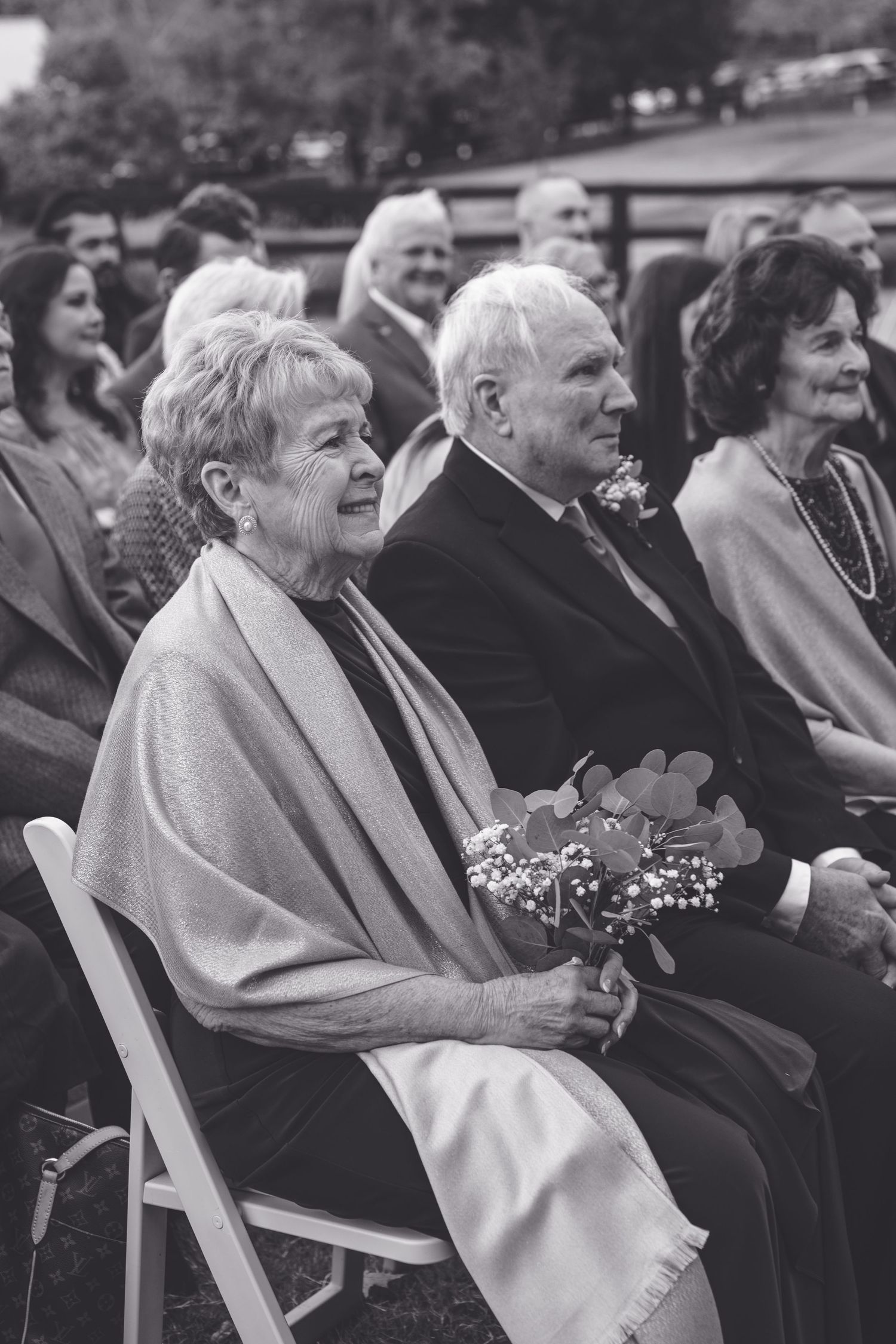 Wedding guests seated in white chairs share joyful reactions during an outdoor ceremony. Southern pines, NC