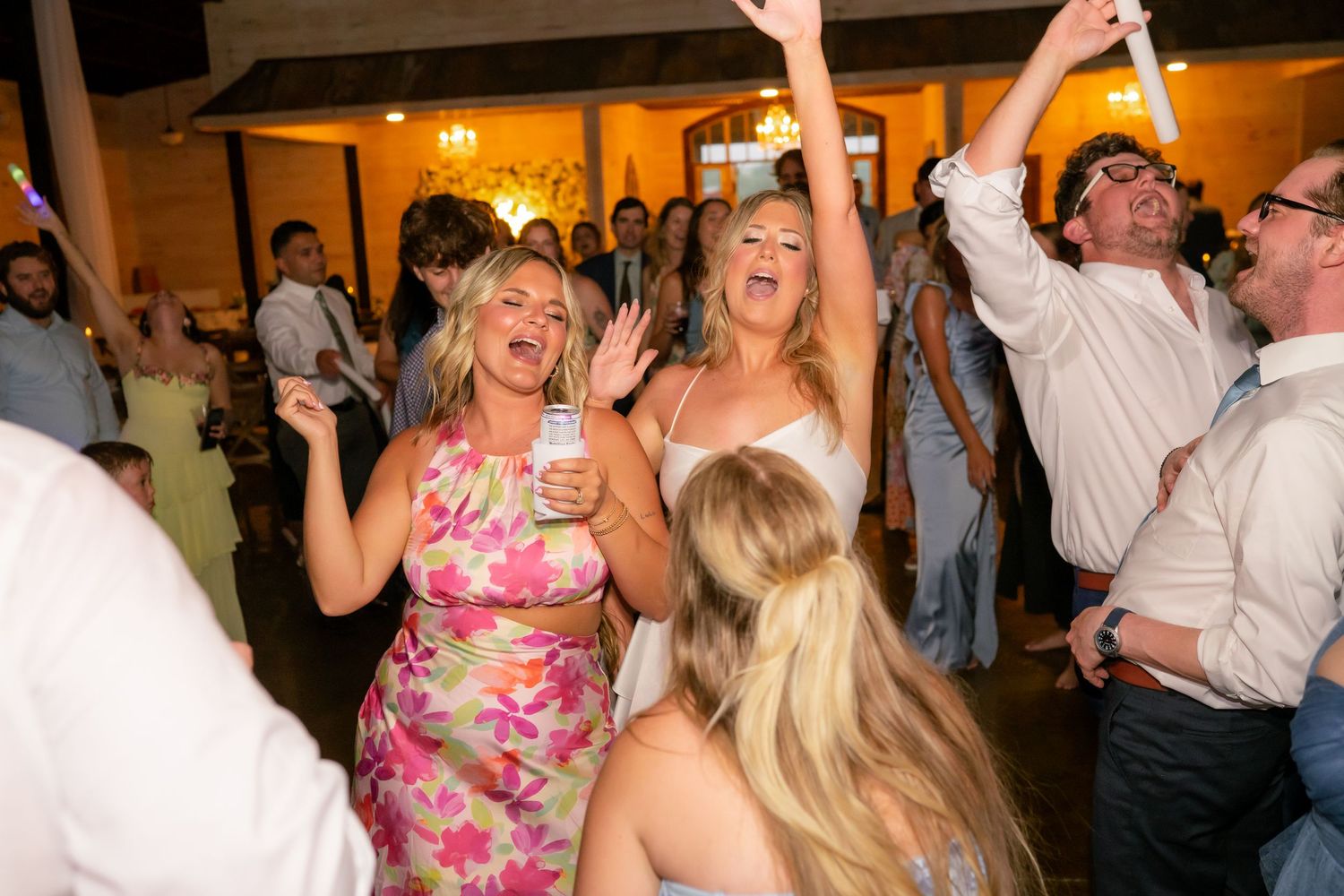 Guests dancing joyfully at a wedding reception, with women in floral dresses celebrating on the dance floor.