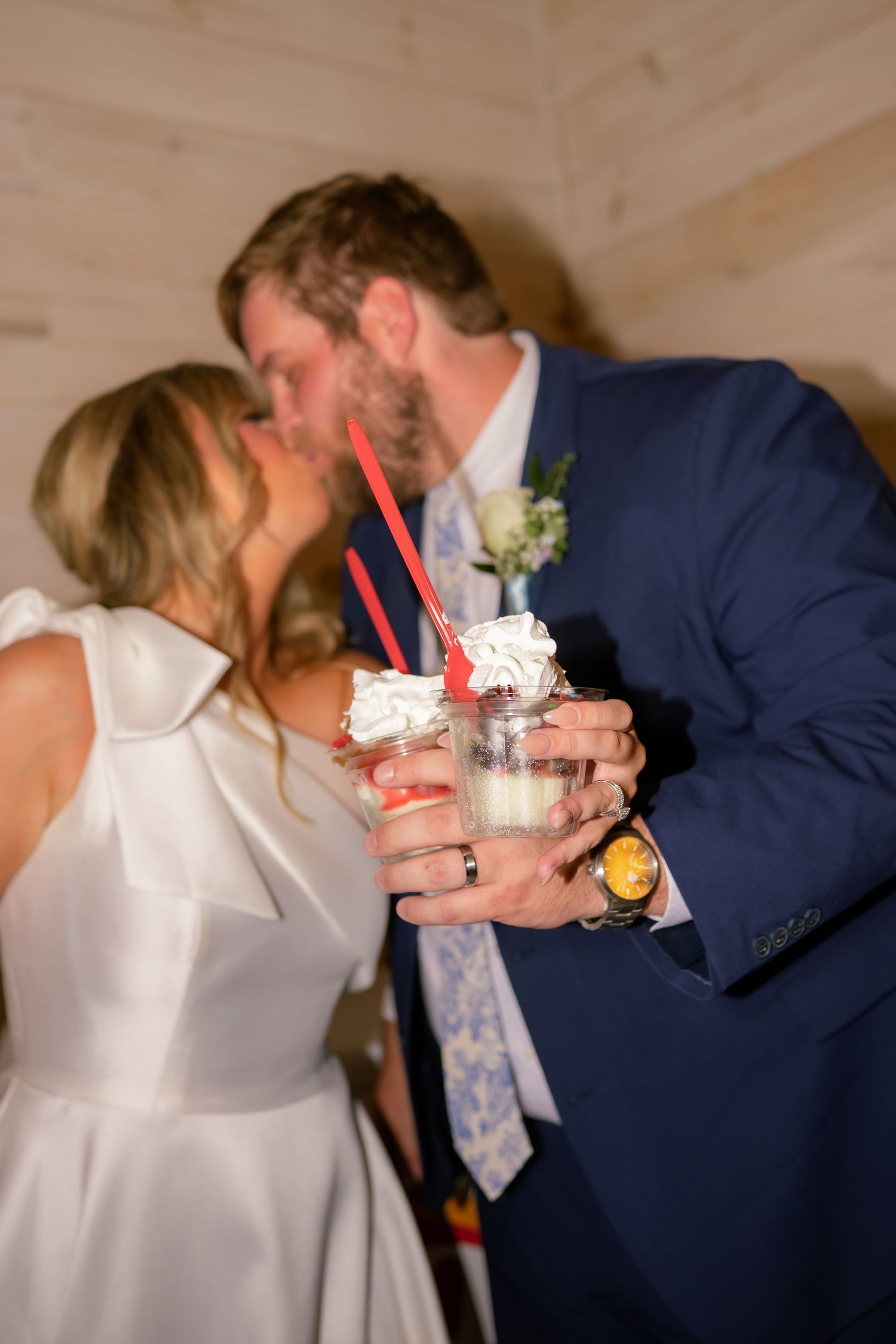 Newlyweds share a kiss while holding festive drinks with red straws at their wedding reception.