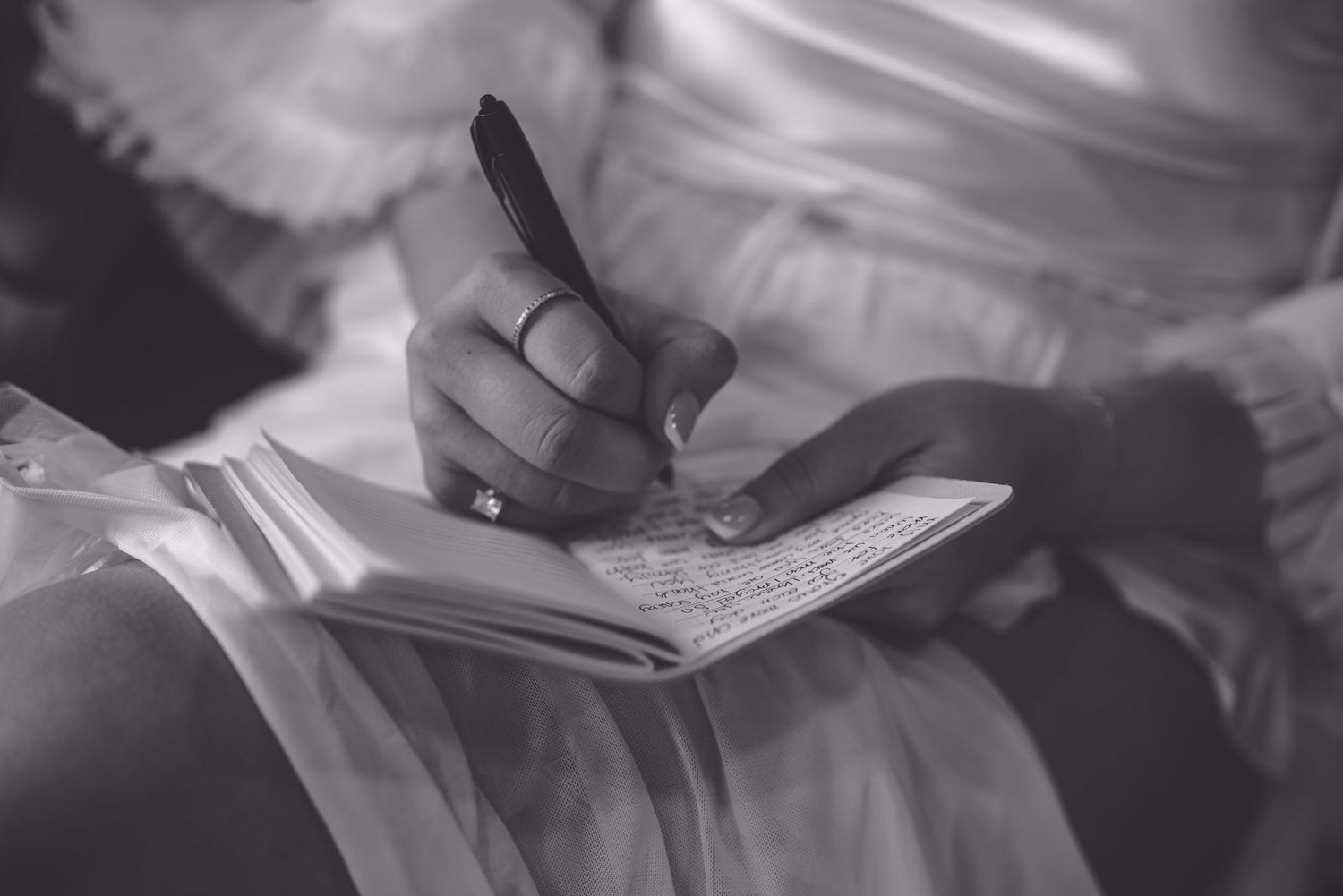 A hand writes in a notebook while wearing formal white attire.