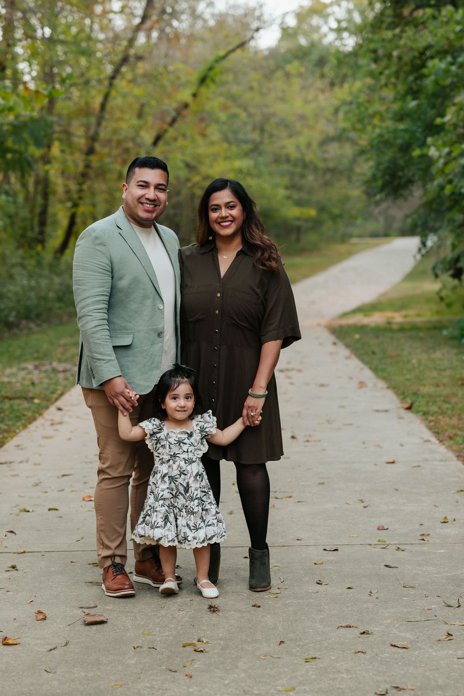 A family poses together on a tree-lined path during a fall photo session.
