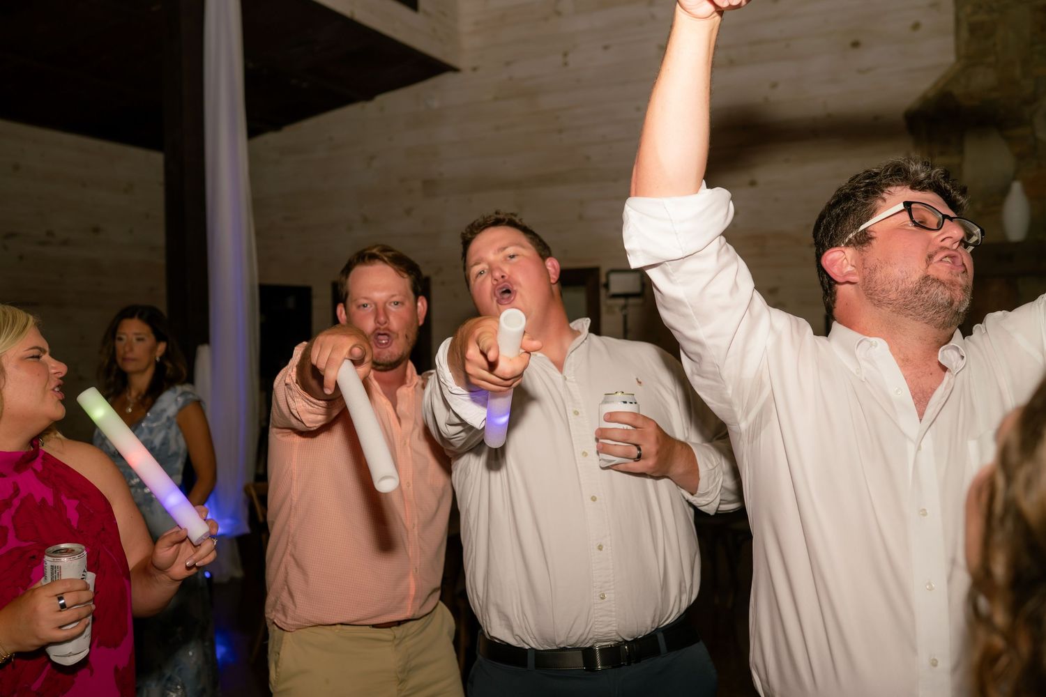 Guests singing and celebrating with glow sticks on wedding reception dance floor.
