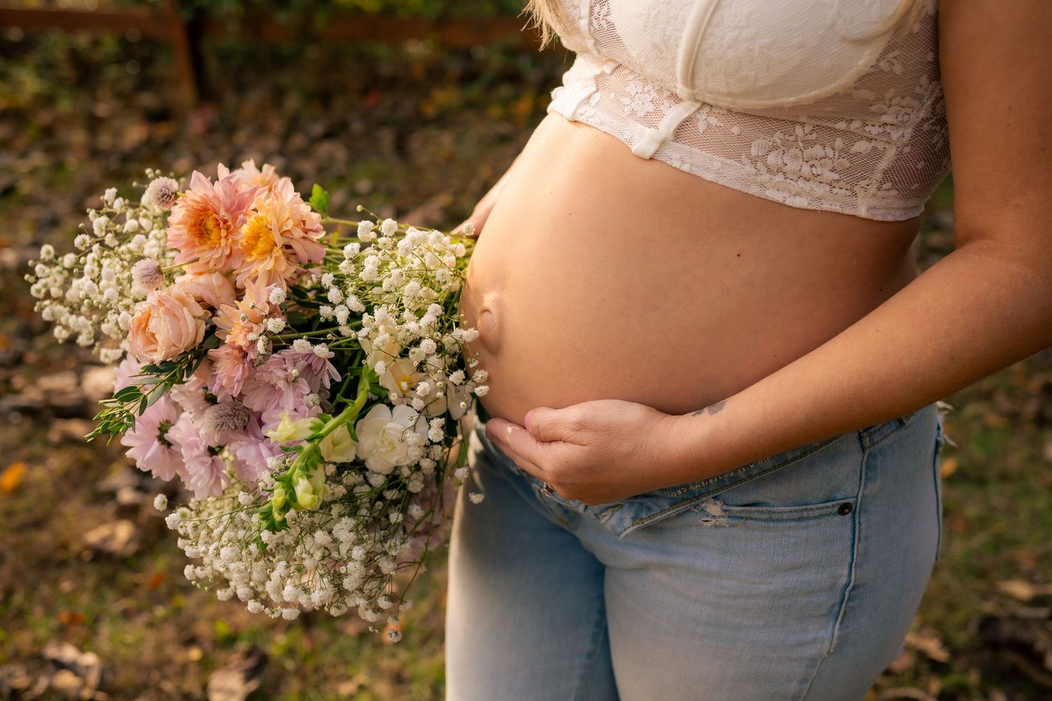 A person in denim jeans holds a delicate bouquet of pink and white flowers against a blurred outdoor background. Southern pines, NC