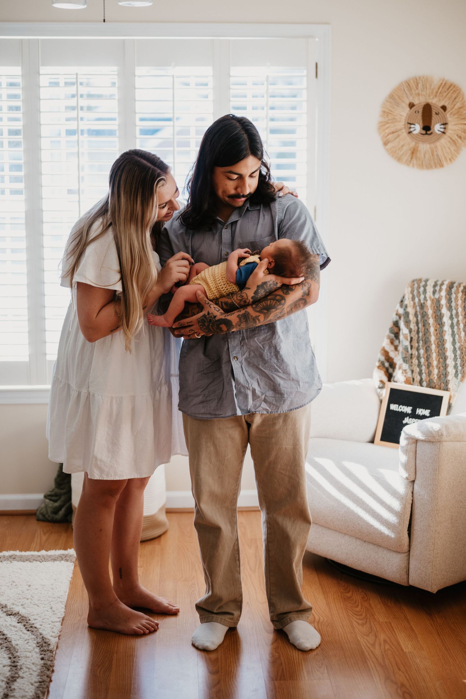 Couple in casual attire gazing lovingly at their newborn in bright modern living room.