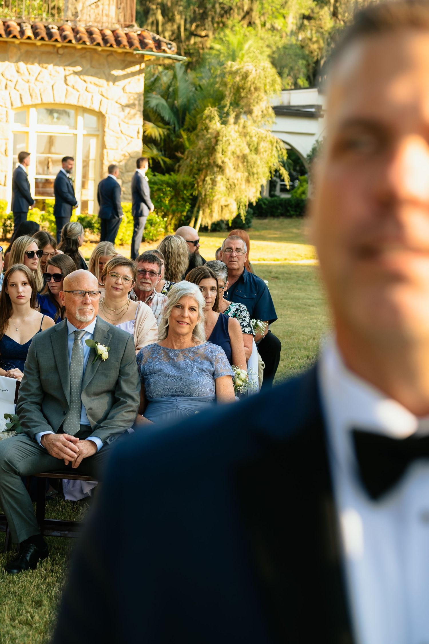 Wedding guests sit outdoors in formal attire during a sunny garden ceremony. North Carolina Wedding Photographer and videographer