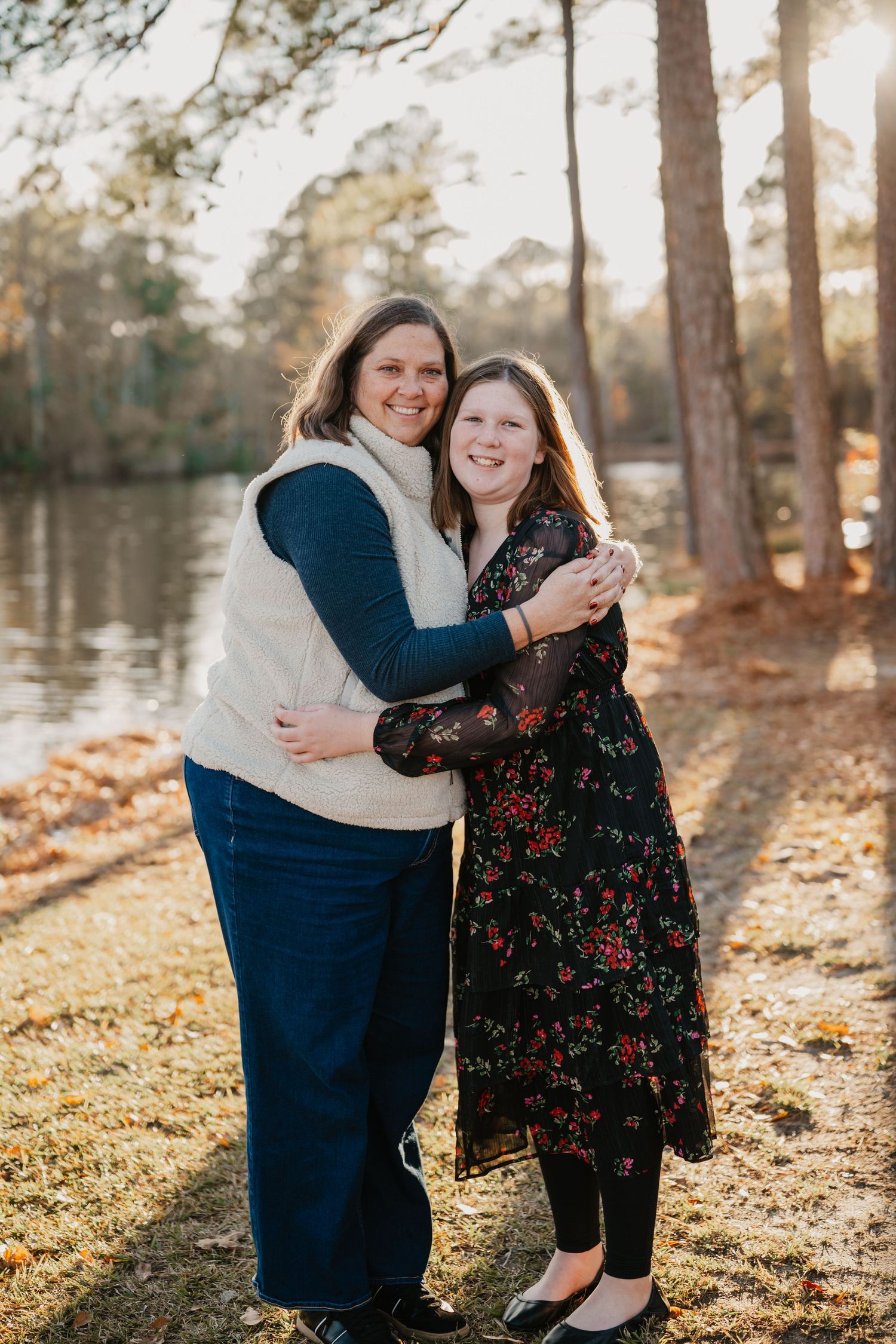 Two people embracing in warm sunlight by lake with autumn trees.