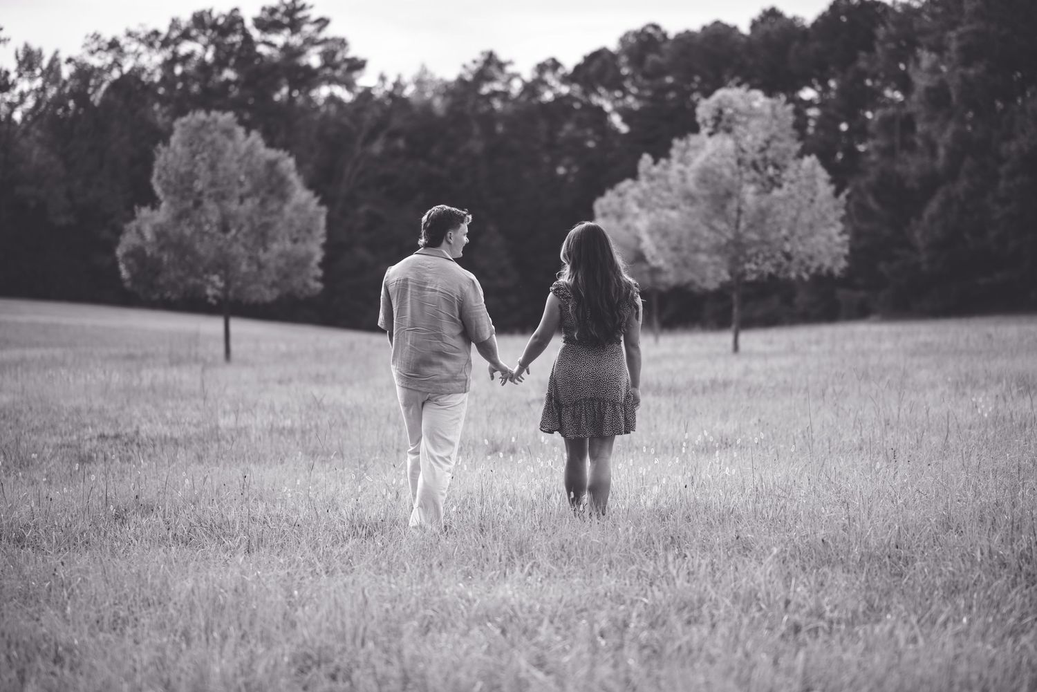 A black and white image of a couple walking hand in hand through an open field.
